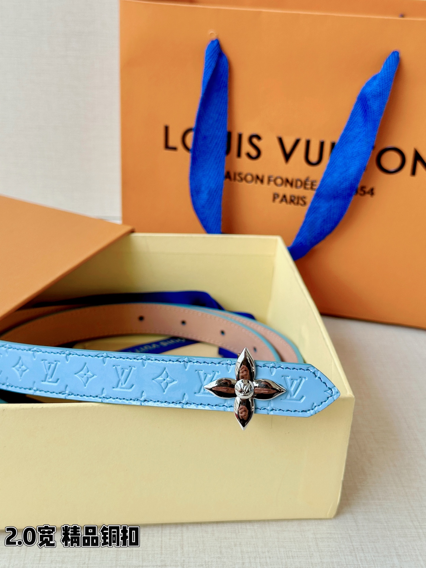 浅蓝色与米白色压纹皮革交织，2.0厘米纤细宽度勾勒腰线。金色铜质四叶花扣头，镌刻经典LV字母与菱形暗纹，