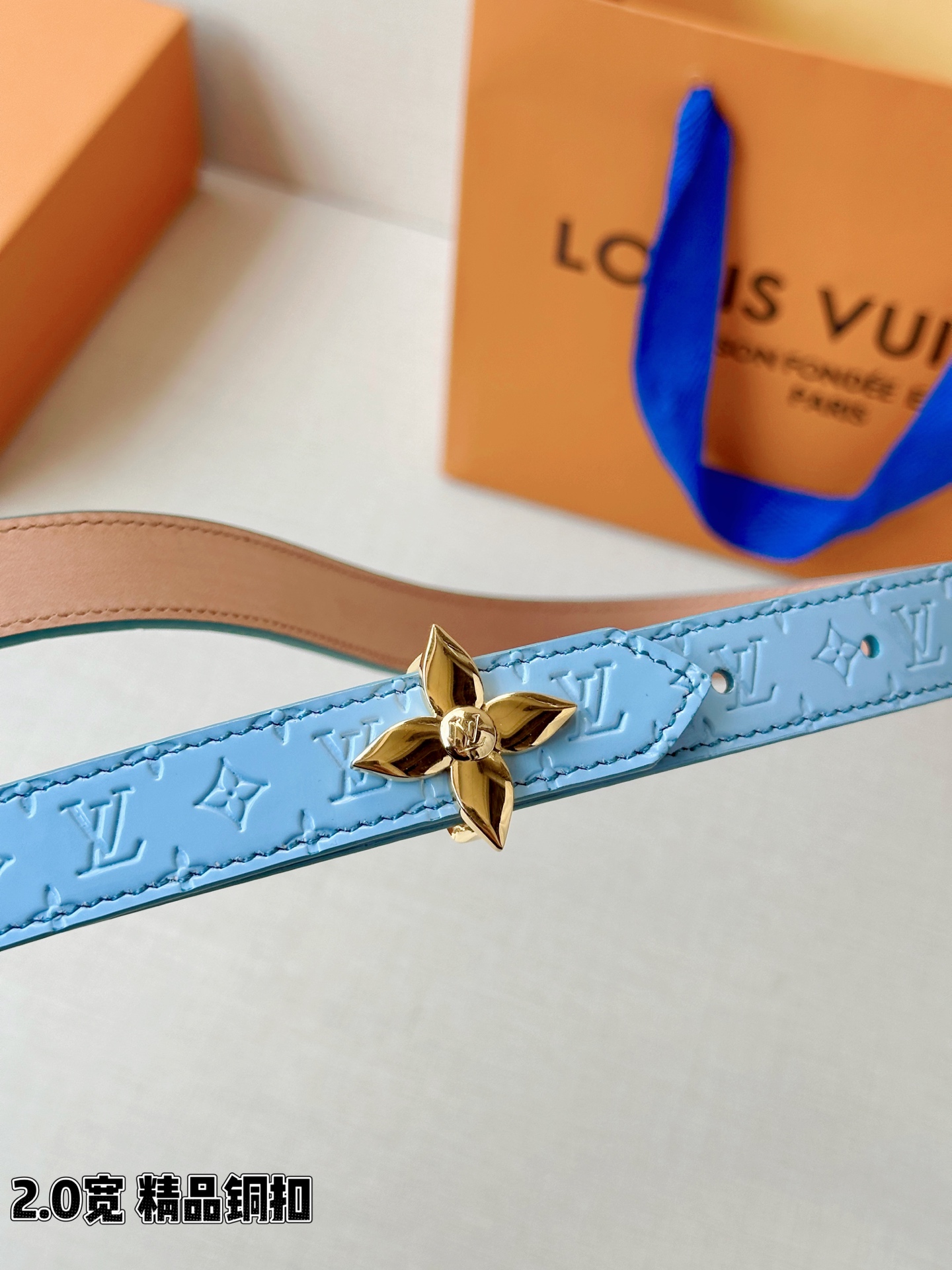 浅蓝色与米白色压纹皮革交织，2.0厘米纤细宽度勾勒腰线。金色铜质四叶花扣头，镌刻经典LV字母与菱形暗纹，