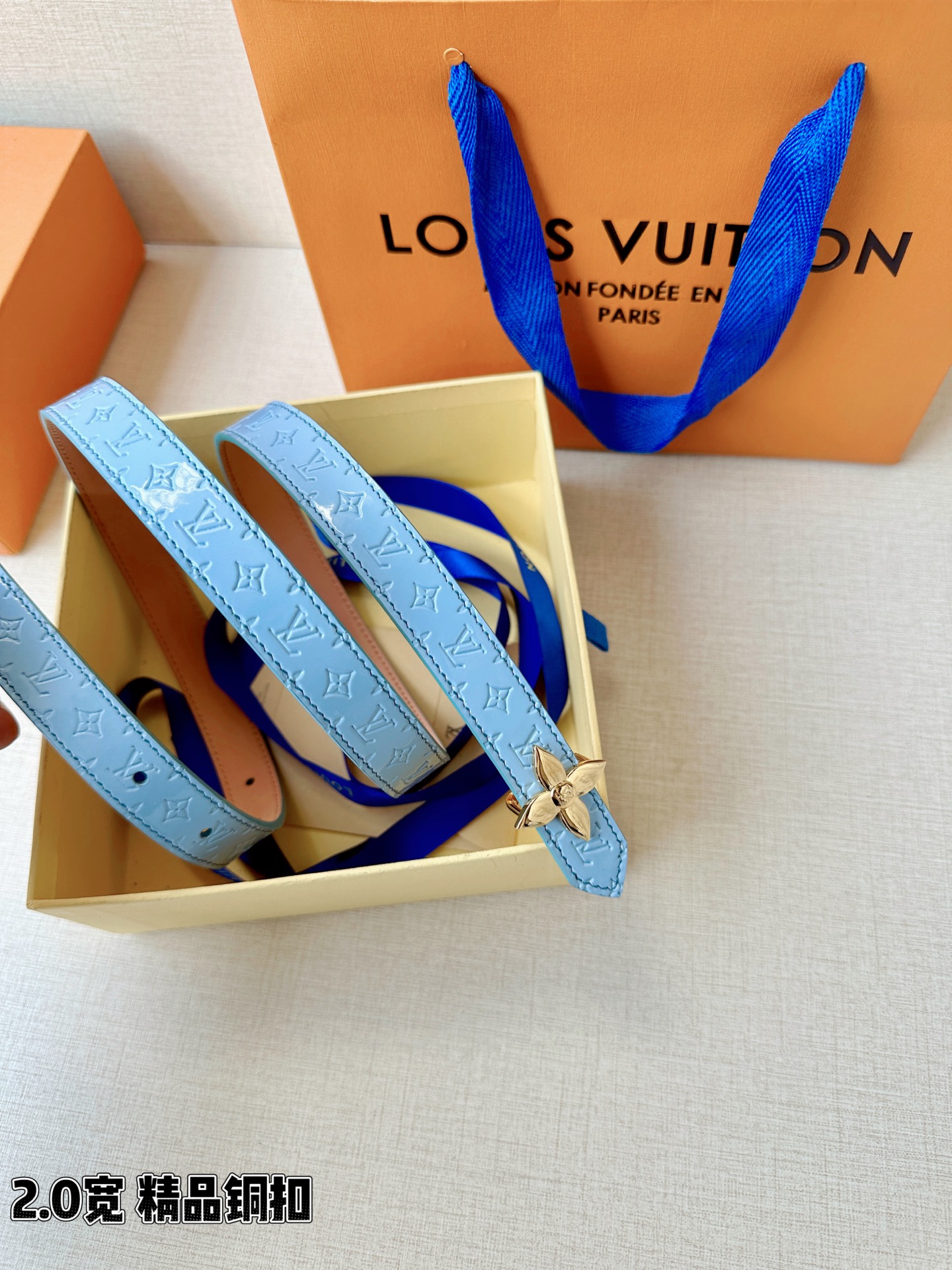浅蓝色与米白色压纹皮革交织，2.0厘米纤细宽度勾勒腰线。金色铜质四叶花扣头，镌刻经典LV字母与菱形暗纹，