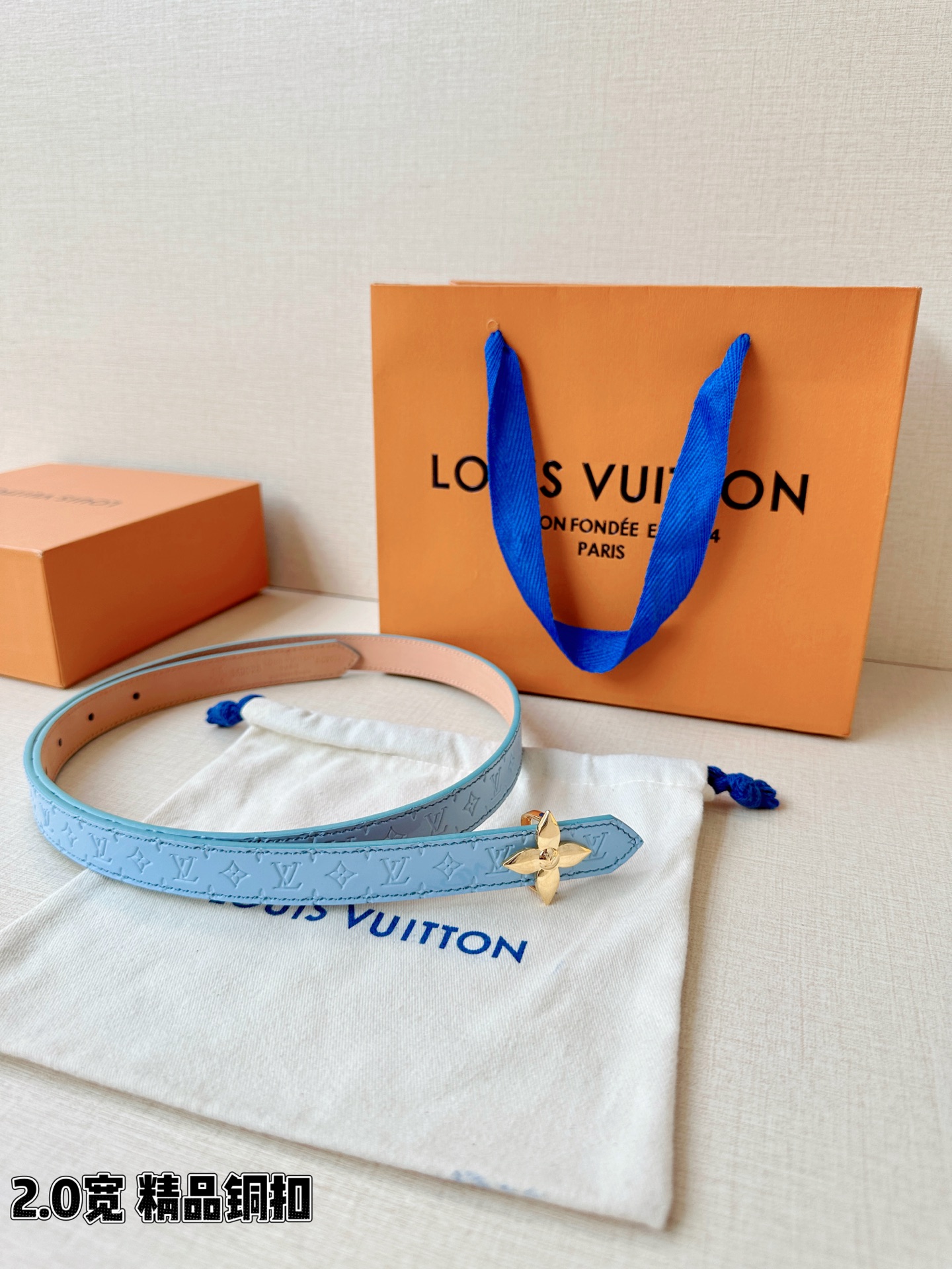 浅蓝色与米白色压纹皮革交织，2.0厘米纤细宽度勾勒腰线。金色铜质四叶花扣头，镌刻经典LV字母与菱形暗纹，