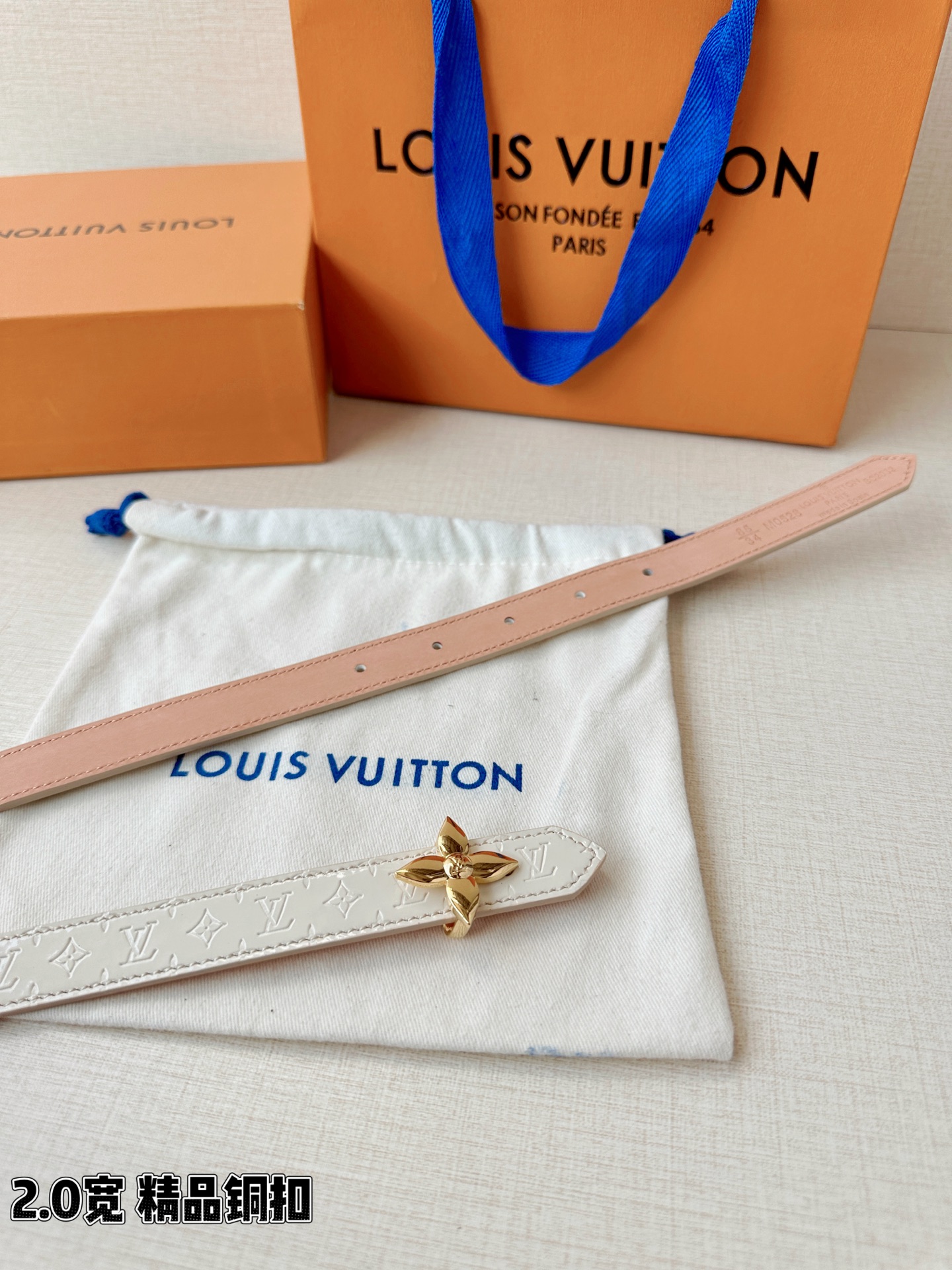 浅蓝色与米白色压纹皮革交织，2.0厘米纤细宽度勾勒腰线。金色铜质四叶花扣头，镌刻经典LV字母与菱形暗纹，