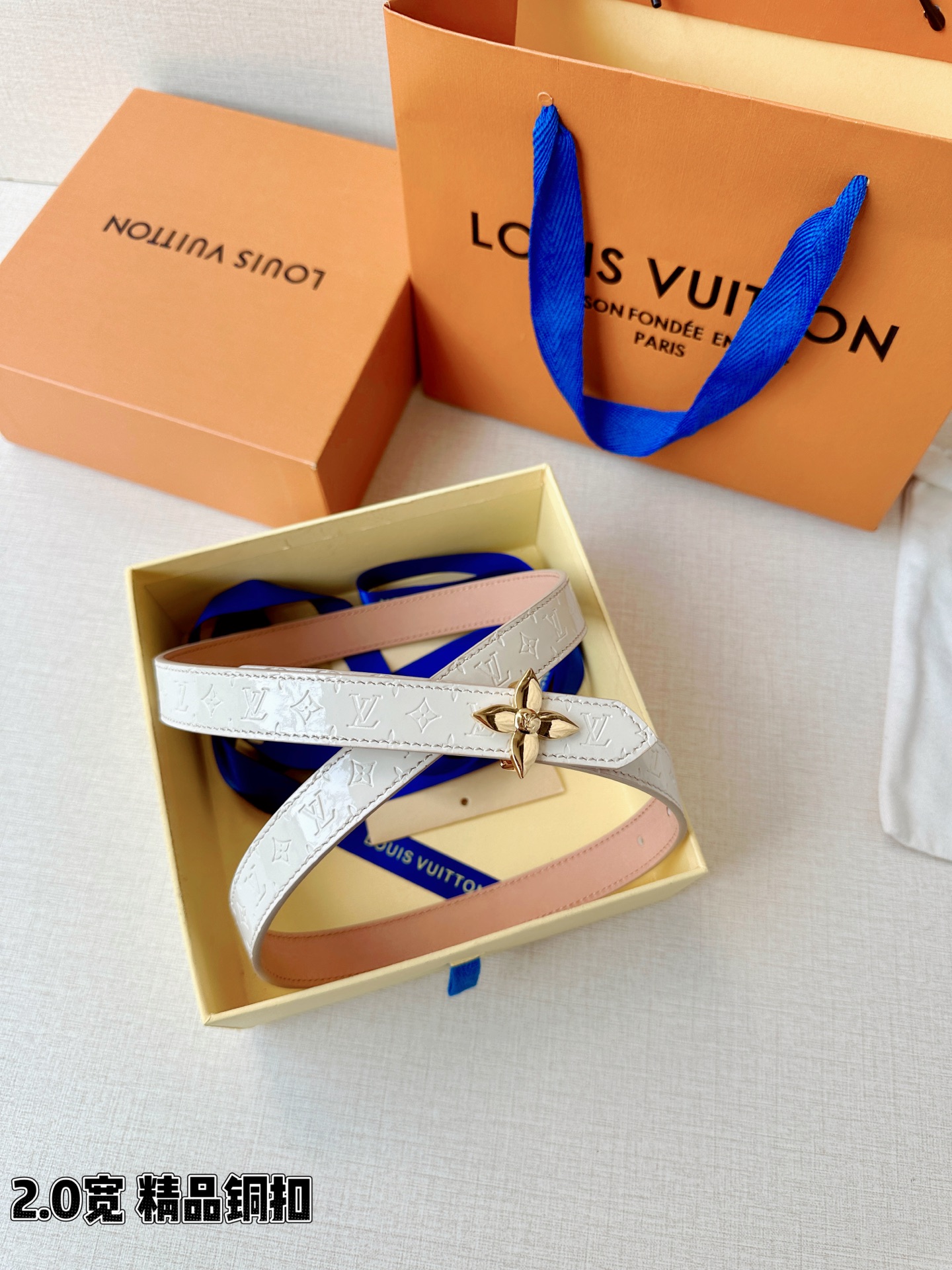 浅蓝色与米白色压纹皮革交织，2.0厘米纤细宽度勾勒腰线。金色铜质四叶花扣头，镌刻经典LV字母与菱形暗纹，