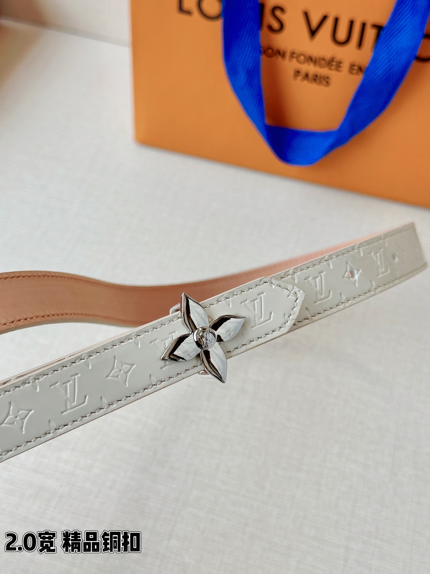 浅蓝色与米白色压纹皮革交织，2.0厘米纤细宽度勾勒腰线。金色铜质四叶花扣头，镌刻经典LV字母与菱形暗纹，
