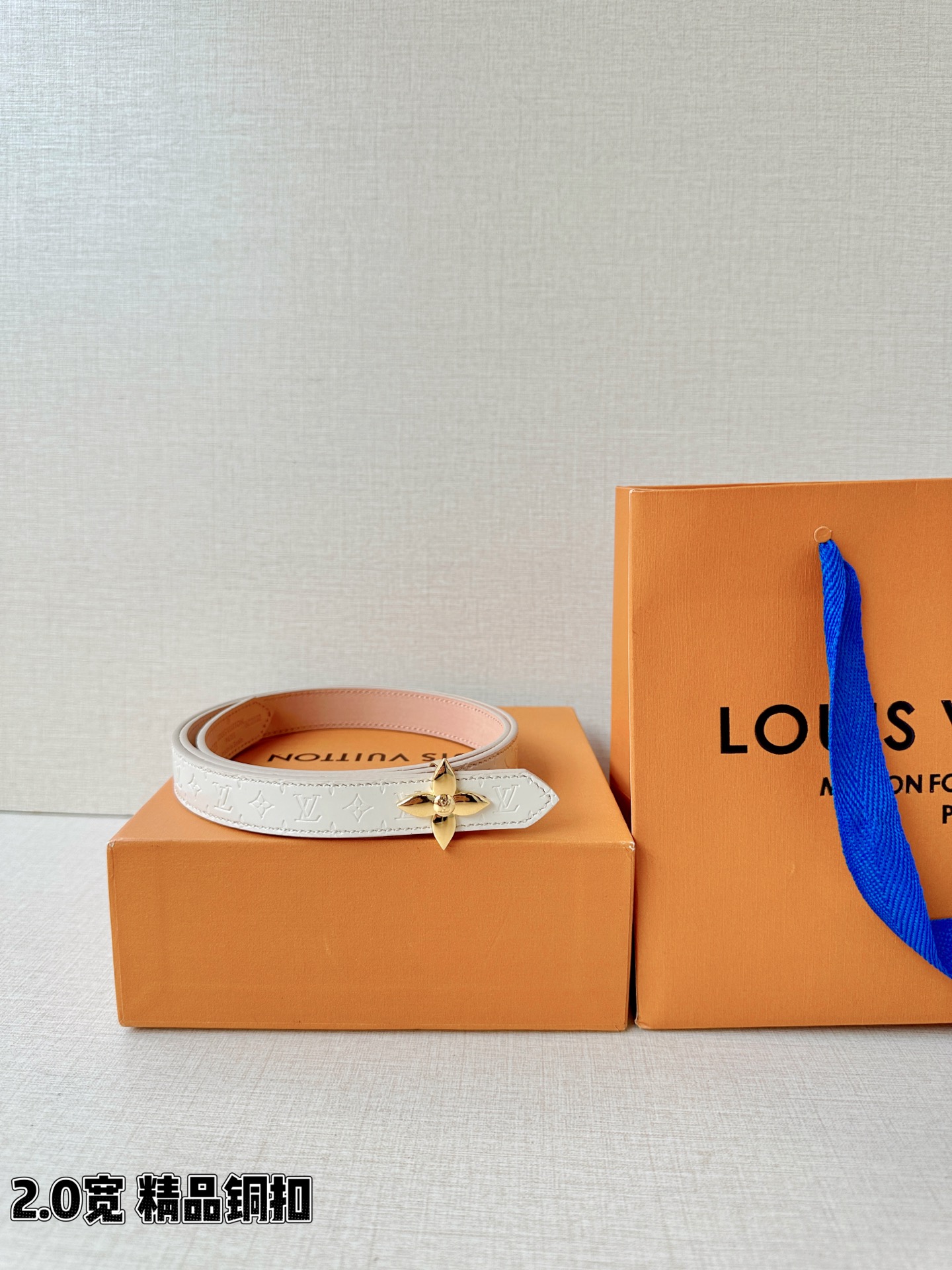 浅蓝色与米白色压纹皮革交织，2.0厘米纤细宽度勾勒腰线。金色铜质四叶花扣头，镌刻经典LV字母与菱形暗纹，