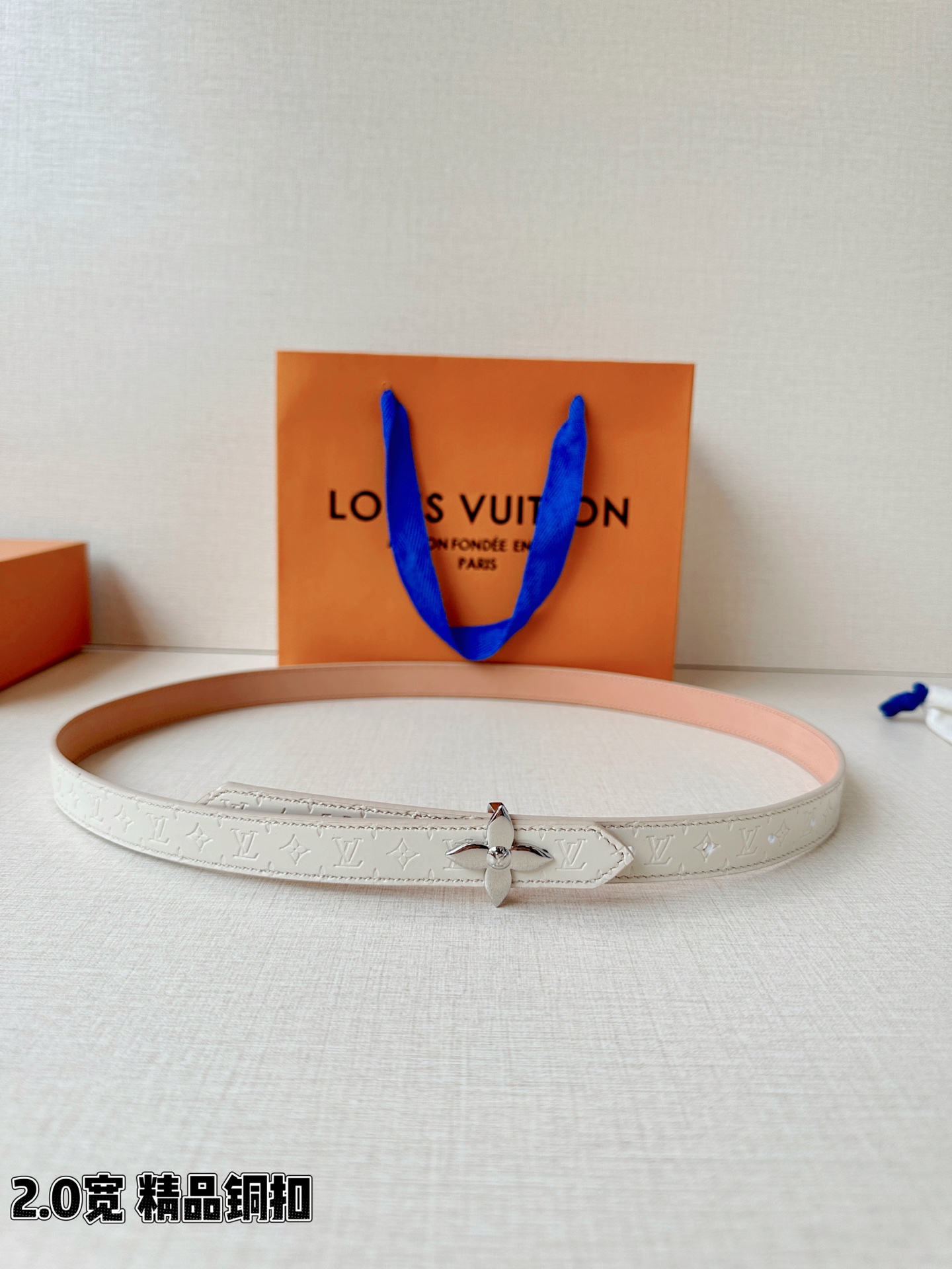 浅蓝色与米白色压纹皮革交织，2.0厘米纤细宽度勾勒腰线。金色铜质四叶花扣头，镌刻经典LV字母与菱形暗纹，