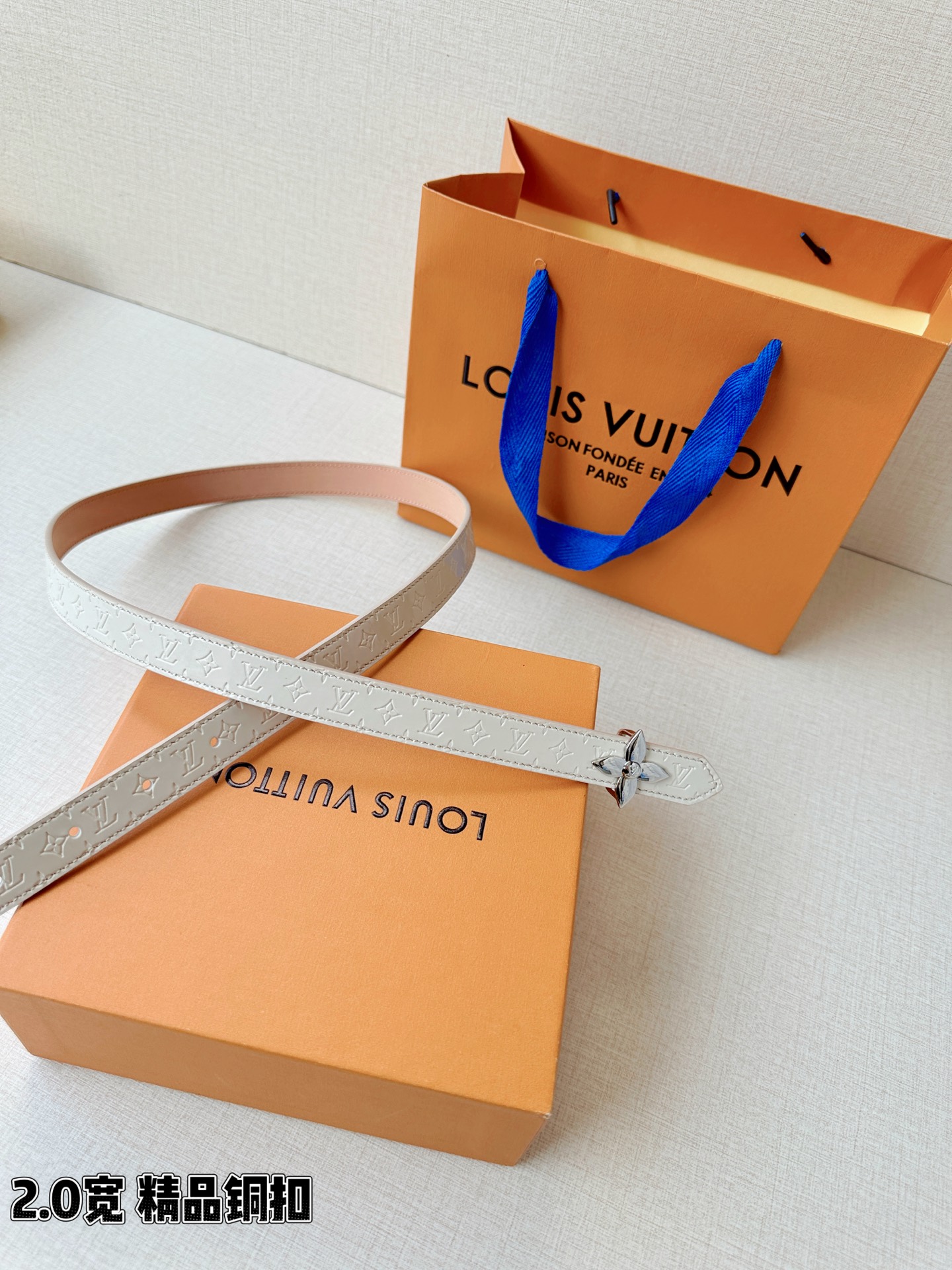 浅蓝色与米白色压纹皮革交织，2.0厘米纤细宽度勾勒腰线。金色铜质四叶花扣头，镌刻经典LV字母与菱形暗纹，
