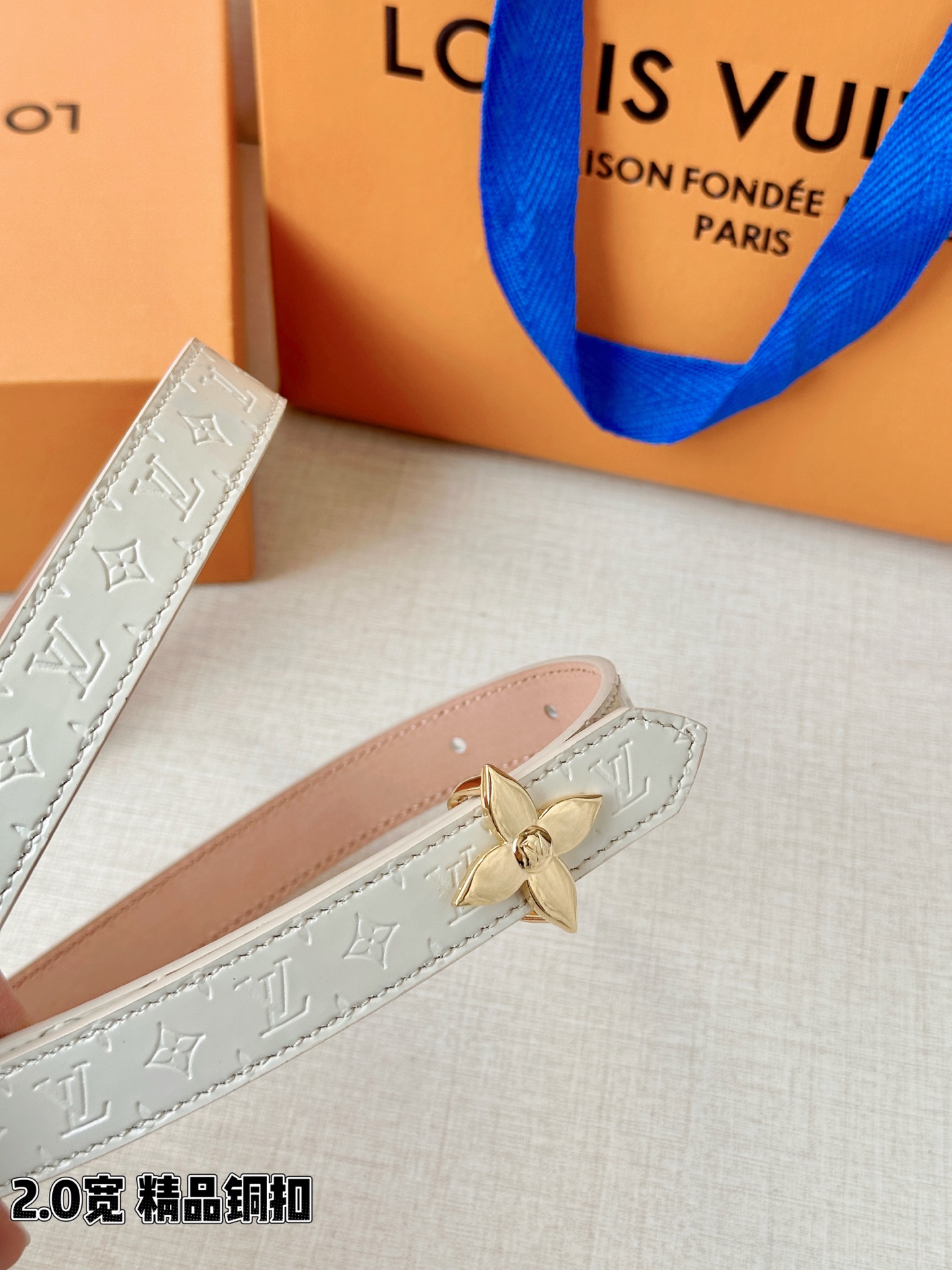 浅蓝色与米白色压纹皮革交织，2.0厘米纤细宽度勾勒腰线。金色铜质四叶花扣头，镌刻经典LV字母与菱形暗纹，