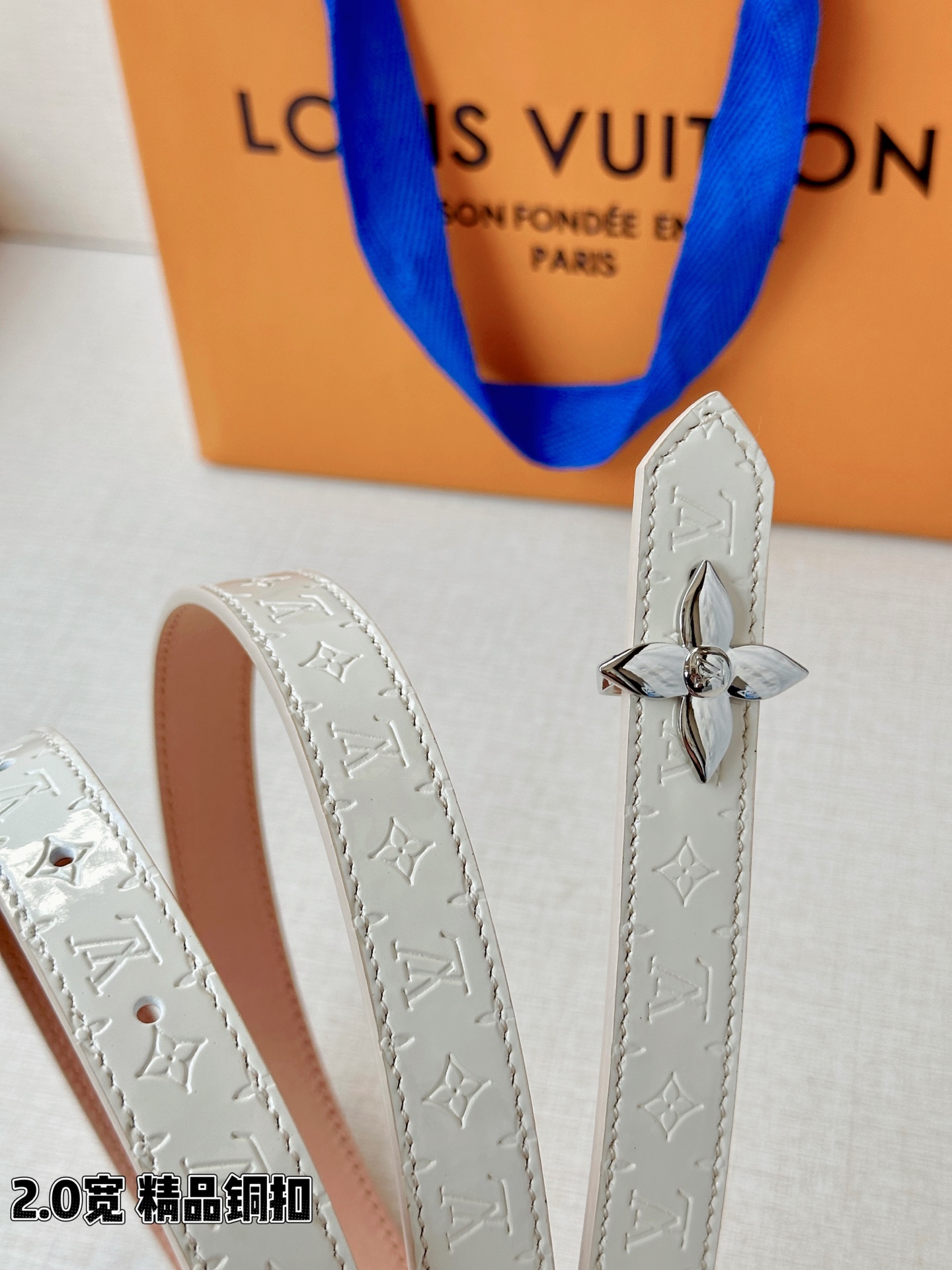 浅蓝色与米白色压纹皮革交织，2.0厘米纤细宽度勾勒腰线。金色铜质四叶花扣头，镌刻经典LV字母与菱形暗纹，