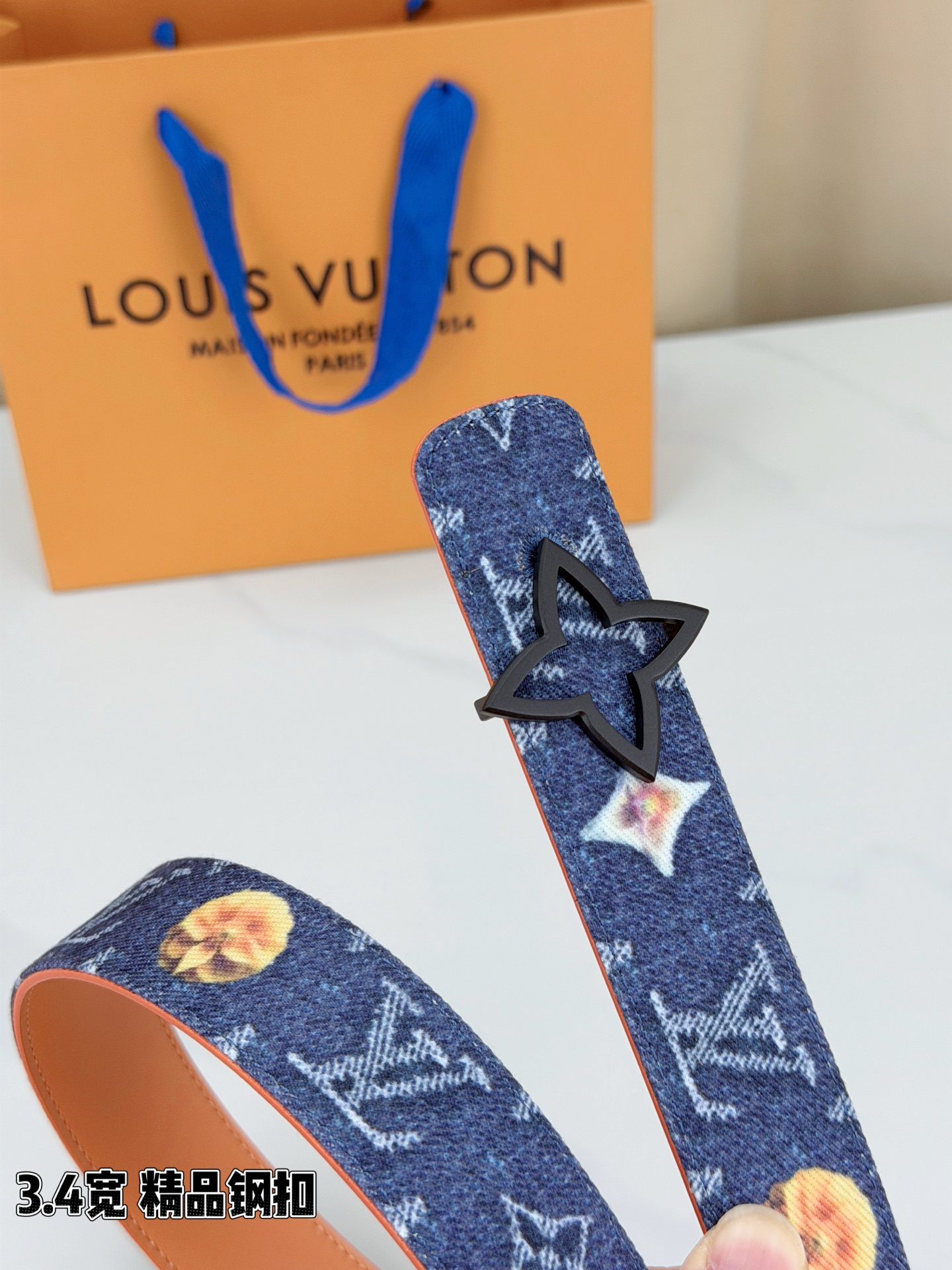 路易威登3.4宽精品钢扣腰带，深蓝牛仔邂逅经典老花，白色LV印记与浅橙花朵交相辉映。镂空四叶花扣金色华贵