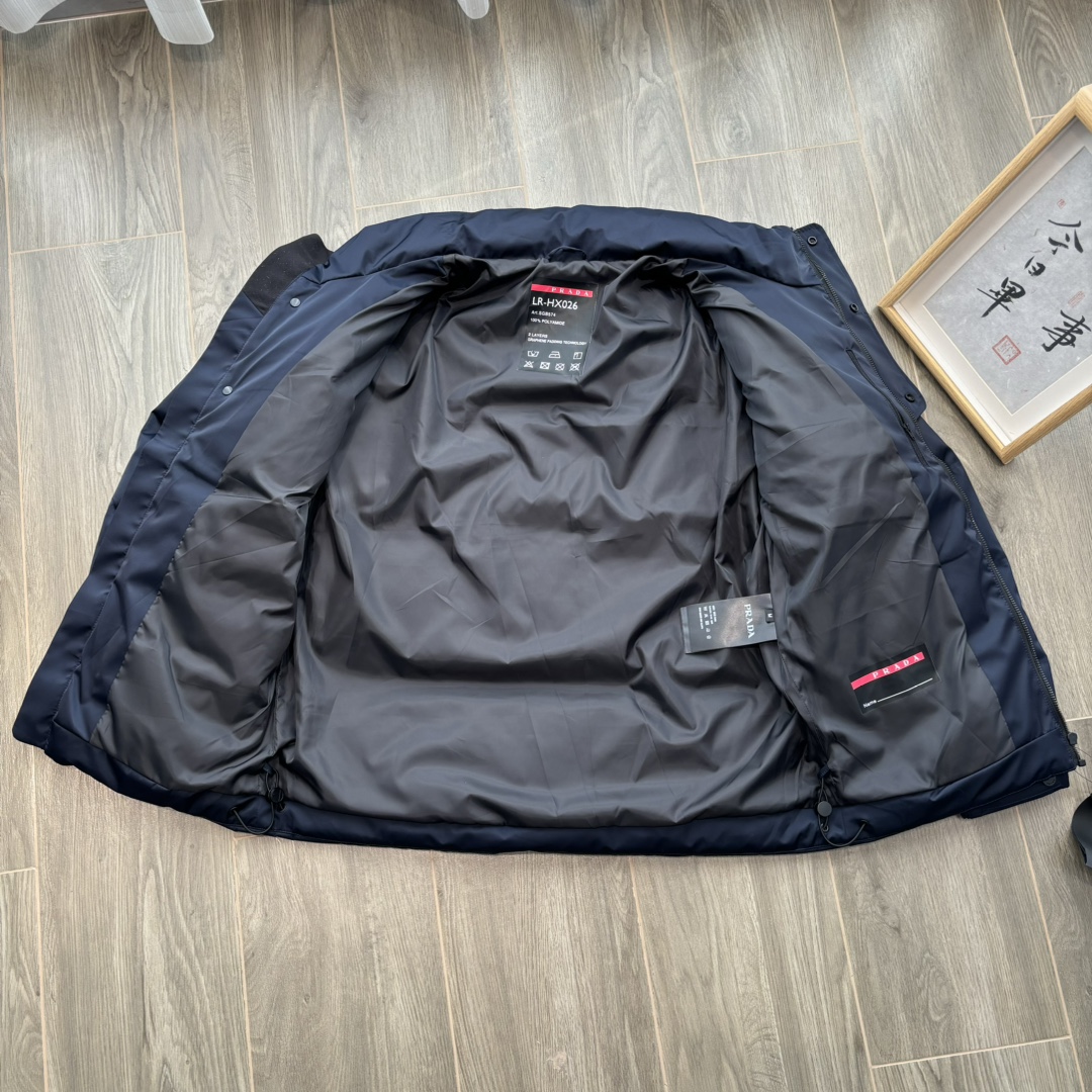 供💰500
PRADA 普拉达 24ss秋冬最新款亮面羽绒服！有品牌独特△三角金属铁标徽章😎
甄选客供100%棉纶材质制作而成，面料拥有极为优越的防水透气性，能抵挡户外寒风雨水的侵蚀，面料触感更是无人能敌
非常的柔软爽滑有光泽！能给你带来舒适的穿着体验！
内里填充物含绒量90%，均经过严格的挑选工序
其蓬松感与与回弹性都极为优越，御寒性能更是毋庸置疑！
客供定制金属拉链与辅料，拉链采用高端压胶工艺处理！
双侧斜插拉链口袋，客供品牌字母刻印拉链头
无处不在彰显大牌气场，连帽设计（🉑拆卸）、简约大气、怎么穿怎么好看 ！双层内衬不出绒高密度防水布料
防风系数超强，蓬松度和保暖性极佳！真正的牛货！走高端的必推！
颜色：黑色 藏青色 

           M	    L	 XL	   2XL	3XL
后中长	71.5  72.5  	74.5  76.5	78.5
胸围	124	   128	132	   136	140
下摆围	113	   117	121	   125	129
肩袖长	78	   79	 80	    81.5  82.5
领围	63.5  63.5   65	    65.5  66.5