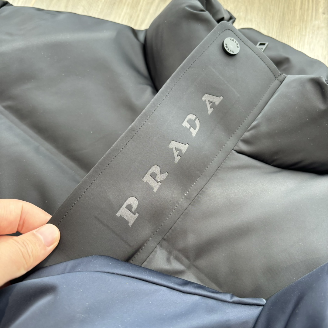 供💰500
PRADA 普拉达 24ss秋冬最新款亮面羽绒服！有品牌独特△三角金属铁标徽章😎
甄选客供100%棉纶材质制作而成，面料拥有极为优越的防水透气性，能抵挡户外寒风雨水的侵蚀，面料触感更是无人能敌
非常的柔软爽滑有光泽！能给你带来舒适的穿着体验！
内里填充物含绒量90%，均经过严格的挑选工序
其蓬松感与与回弹性都极为优越，御寒性能更是毋庸置疑！
客供定制金属拉链与辅料，拉链采用高端压胶工艺处理！
双侧斜插拉链口袋，客供品牌字母刻印拉链头
无处不在彰显大牌气场，连帽设计（🉑拆卸）、简约大气、怎么穿怎么好看 ！双层内衬不出绒高密度防水布料
防风系数超强，蓬松度和保暖性极佳！真正的牛货！走高端的必推！
颜色：黑色 藏青色 

           M	    L	 XL	   2XL	3XL
后中长	71.5  72.5  	74.5  76.5	78.5
胸围	124	   128	132	   136	140
下摆围	113	   117	121	   125	129
肩袖长	78	   79	 80	    81.5  82.5
领围	63.5  63.5   65	    65.5  66.5