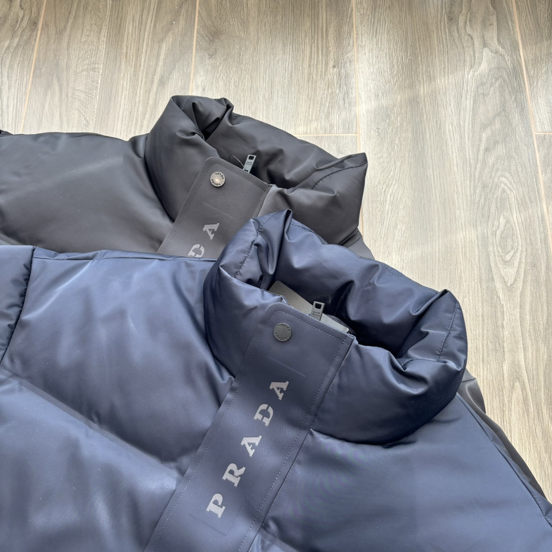 供💰500
PRADA 普拉达 24ss秋冬最新款亮面羽绒服！有品牌独特△三角金属铁标徽章😎
甄选客供100%棉纶材质制作而成，面料拥有极为优越的防水透气性，能抵挡户外寒风雨水的侵蚀，面料触感更是无人能敌
非常的柔软爽滑有光泽！能给你带来舒适的穿着体验！
内里填充物含绒量90%，均经过严格的挑选工序
其蓬松感与与回弹性都极为优越，御寒性能更是毋庸置疑！
客供定制金属拉链与辅料，拉链采用高端压胶工艺处理！
双侧斜插拉链口袋，客供品牌字母刻印拉链头
无处不在彰显大牌气场，连帽设计（🉑拆卸）、简约大气、怎么穿怎么好看 ！双层内衬不出绒高密度防水布料
防风系数超强，蓬松度和保暖性极佳！真正的牛货！走高端的必推！
颜色：黑色 藏青色 

           M	    L	 XL	   2XL	3XL
后中长	71.5  72.5  	74.5  76.5	78.5
胸围	124	   128	132	   136	140
下摆围	113	   117	121	   125	129
肩袖长	78	   79	 80	    81.5  82.5
领围	63.5  63.5   65	    65.5  66.5