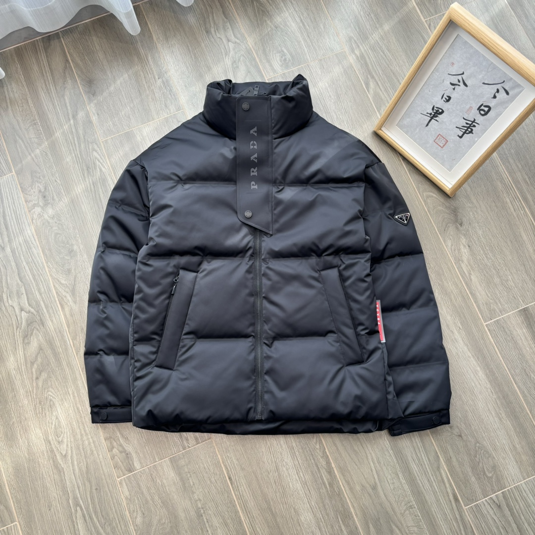 供💰500
PRADA 普拉达 24ss秋冬最新款亮面羽绒服！有品牌独特△三角金属铁标徽章😎
甄选客供100%棉纶材质制作而成，面料拥有极为优越的防水透气性，能抵挡户外寒风雨水的侵蚀，面料触感更是无人能敌
非常的柔软爽滑有光泽！能给你带来舒适的穿着体验！
内里填充物含绒量90%，均经过严格的挑选工序
其蓬松感与与回弹性都极为优越，御寒性能更是毋庸置疑！
客供定制金属拉链与辅料，拉链采用高端压胶工艺处理！
双侧斜插拉链口袋，客供品牌字母刻印拉链头
无处不在彰显大牌气场，连帽设计（🉑拆卸）、简约大气、怎么穿怎么好看 ！双层内衬不出绒高密度防水布料
防风系数超强，蓬松度和保暖性极佳！真正的牛货！走高端的必推！
颜色：黑色 藏青色 

           M	    L	 XL	   2XL	3XL
后中长	71.5  72.5  	74.5  76.5	78.5
胸围	124	   128	132	   136	140
下摆围	113	   117	121	   125	129
肩袖长	78	   79	 80	    81.5  82.5
领围	63.5  63.5   65	    65.5  66.5