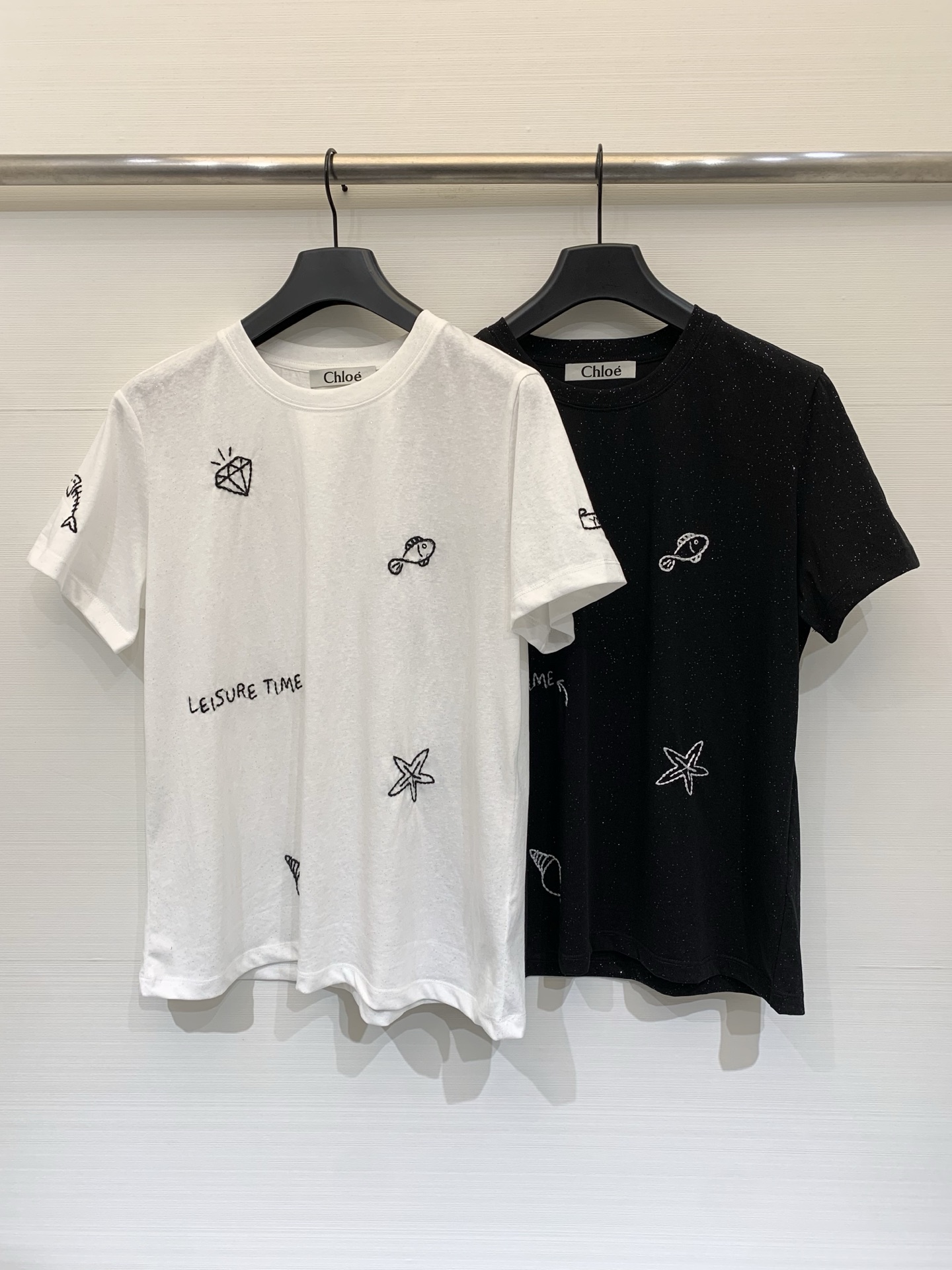 NO:800867,Chloé 26 Spring and Summer New Black and White Glitter Childlike Embroidered T-shirt, classic round neck regular short-sleeved T-shirt, the body is covered with exquisite hand-embroidered patterns, including diamonds, small fish, starfish, conch and other marine life elements, full of playful artistic sense and summer vacation atmosphere, the fabric is woven with delicate glitter/shine silk material, showing a low-key luster under the light, improving the overall sophistication  Two-color SML,,chloe,T-shirt,tees,t-shirt,19860909Chloé 26春夏新款 黑白闪粉童趣刺绣T恤,经典圆领常规版短袖T恤,衣身布满精致的手工刺绣图案,包含钻石、小鱼、海星、海螺等海洋生物元素,充满俏皮的艺术感与夏日度假氛围,面料中织入了细腻的闪粉/亮丝材质,在光线下呈现低调的光泽感,提升整体精致度 两色SML,,chloe,T-shirt,tees，t-shirt,,Women's clothing