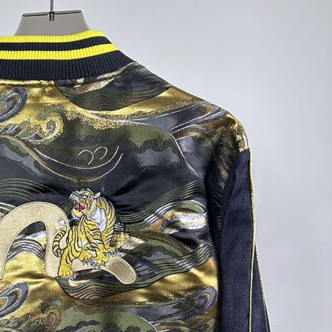 P180
款号：Z49
重磅来袭，新款推荐，EVISU（福神）外套，三标齐全，采用经典棒球服款式，整体以牛仔面料打造，领口、袖口和下摆处有亮眼的黄色条纹装饰，增添活力与复古感。正面有醒目的 “EVISU” 品牌标识，彰显品牌特色。
尤为吸睛的是背面，运用了极具艺术感的印花设计，海浪与老虎等元素结合，色彩搭配华丽，既带有日式传统美学韵味，又充满潮流个性，是将街头风格与品牌经典元素巧妙融合的单品，适合追求独特时尚感的穿搭者。
S-XL