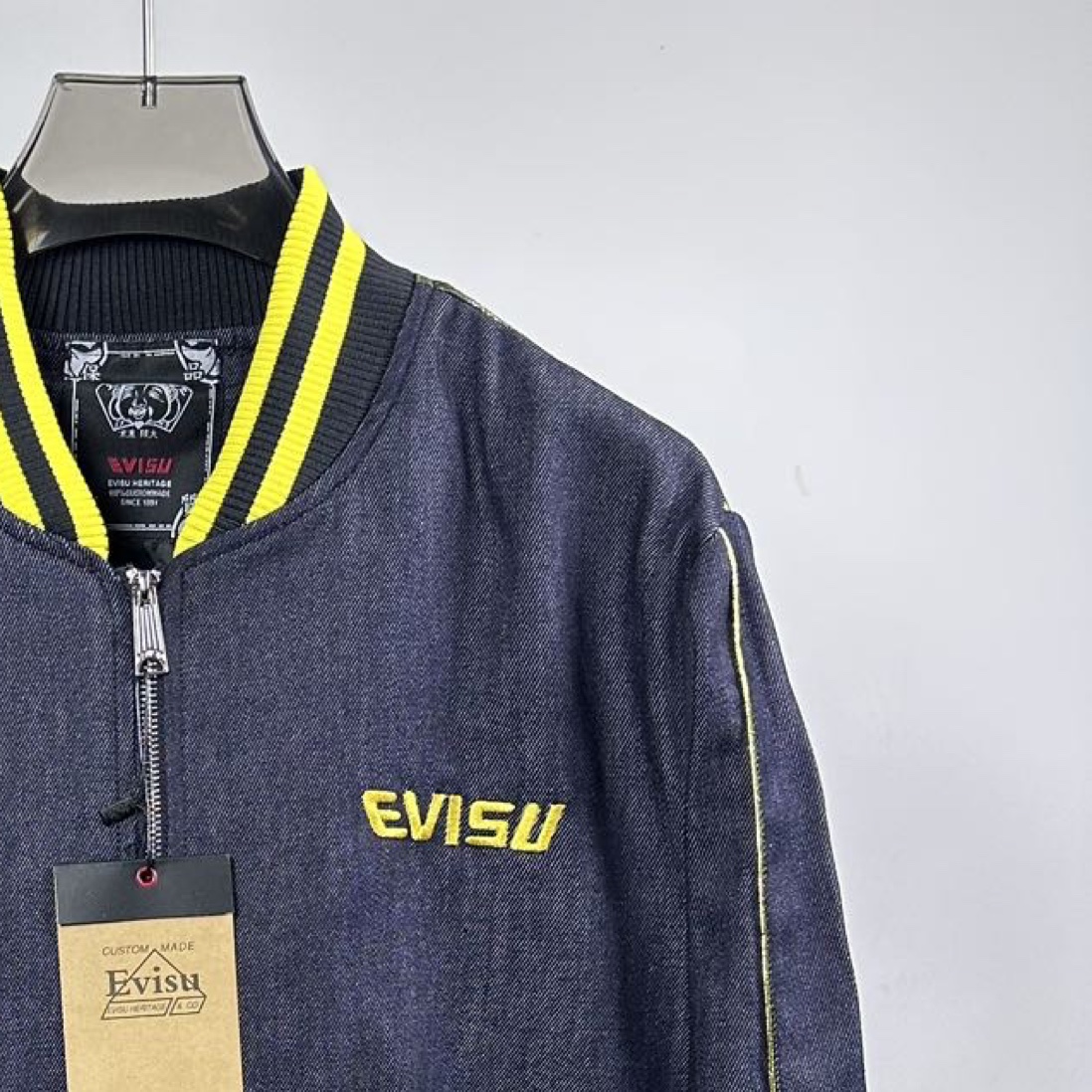 P180
款号：Z49
重磅来袭，新款推荐，EVISU（福神）外套，三标齐全，采用经典棒球服款式，整体以牛仔面料打造，领口、袖口和下摆处有亮眼的黄色条纹装饰，增添活力与复古感。正面有醒目的 “EVISU” 品牌标识，彰显品牌特色。
尤为吸睛的是背面，运用了极具艺术感的印花设计，海浪与老虎等元素结合，色彩搭配华丽，既带有日式传统美学韵味，又充满潮流个性，是将街头风格与品牌经典元素巧妙融合的单品，适合追求独特时尚感的穿搭者。
S-XL