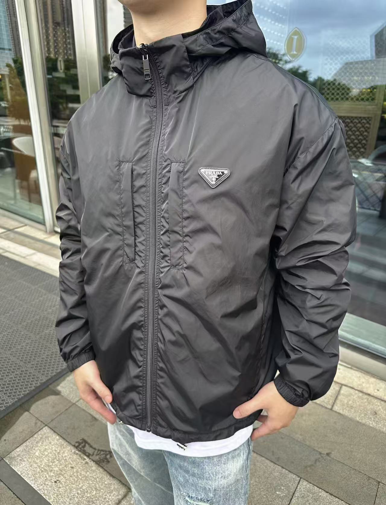 NO:506104,.PRADA recycled nylon double-sided jacket fabric selection The brand's signature recycled nylon fabric is comparable to traditional nylon, with high strength, tear resistance, wear resistance and other characteristics. Its texture is light and waterproof, and is suitable for multiple scenarios. Its wrinkle and quick drying are also easy to maintain and maintain daily. Process: Wrap parts with oblique cut cloth strips, with width controlled at about 0.4CM. Align the edges of the two layers of fabric and fold and sew the seams, and then fix them through the 'anchor point'. It forms no burrs on both sides of the inside and outside, and all seams are completely wrapped, while preventing the undesirable experience of easy sliding relative to wear. Auxiliary materials are compared with custom triangle marks, comparing with custom hem elastic buckles, comparing with custom hat rope elastic leather head, comparing with custom zipper head SIZE: S M L XL,,prada, jackets &  coats, hats, alexander wang19860909.PRADA再生尼龙双面穿夹克 面料选择 选用品牌标志性的再生尼龙面料,与传统尼龙性能相当,具备高强度,抗撕裂,耐磨损等特性.其质地轻盈,同时又具备防水功能适合多场景需求.抗皱,快干的特点也易于日常打理维护. 工艺 用斜裁布条包裹份,宽度控制在0.4CM左右.将两层面料边缘对齐后折叠缝合,缝线隐藏于夹层.再通过“锚定点”固定.形成内外两面均无毛边,所有缝份完全包裹,同时防止穿着中易相对滑动的不良体验. 辅料一比一定制三角标 一比一定制下摆松紧扣 一比一定制帽绳松紧皮头 一比一定制拉链头 SIZE: S M L XL,,prada,jackets & coats,hats,alexander wang,Men's clothing