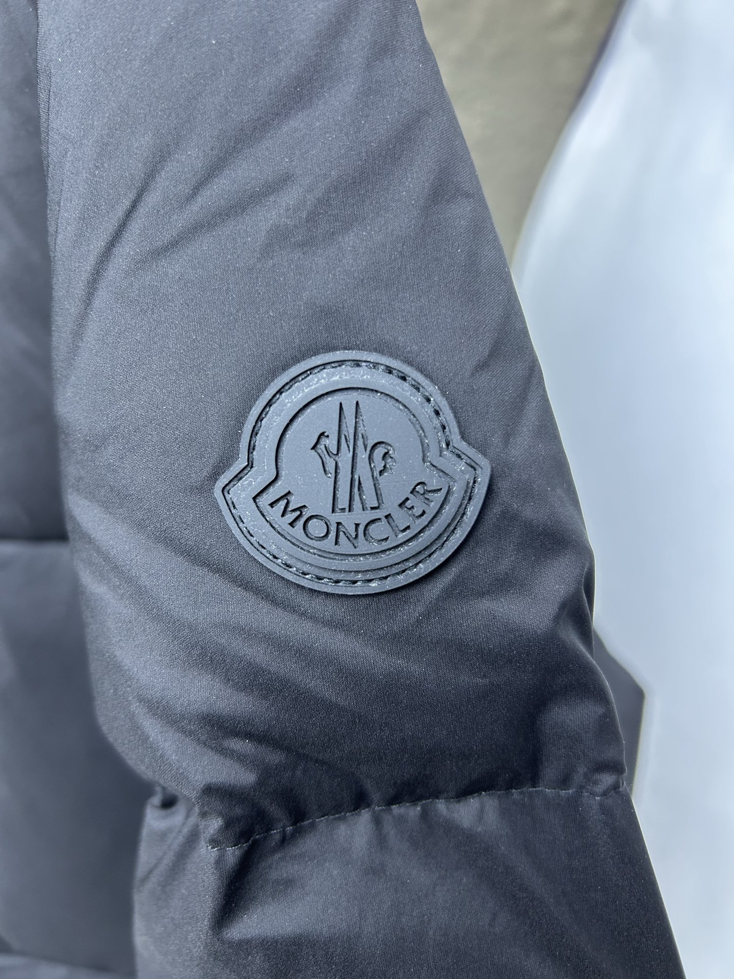 Moncler Fusain short down jacket inspired by racing. Features quilted nylon, lightweight warmth, sleek silhouette, hood, and reflective zipper. Available in black and off-white.-Big cat