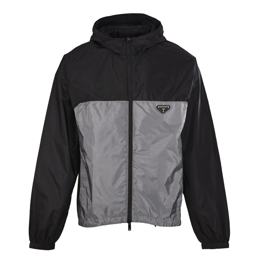 正品级💰480 Prada普拉达PRD 黑灰拼接连帽夹克外套 这款尼龙面料是一种通过回收海洋中的塑料材料制成的再生尼龙织物，竖向嵌线袋与隐藏式拉链的结合，既保留了嵌线袋的实用性和美观性，又通过隐藏式拉链的设计提升了服装的档次感和安全性。设计手法通常出现在高端或注重细节的服装品牌中，能够显著提升服装的品质感和价值感。 小提示⚠ 官网照片与实物有色差，请看专柜买版实拍，原版面料定制才能无色差 Size：S-XL