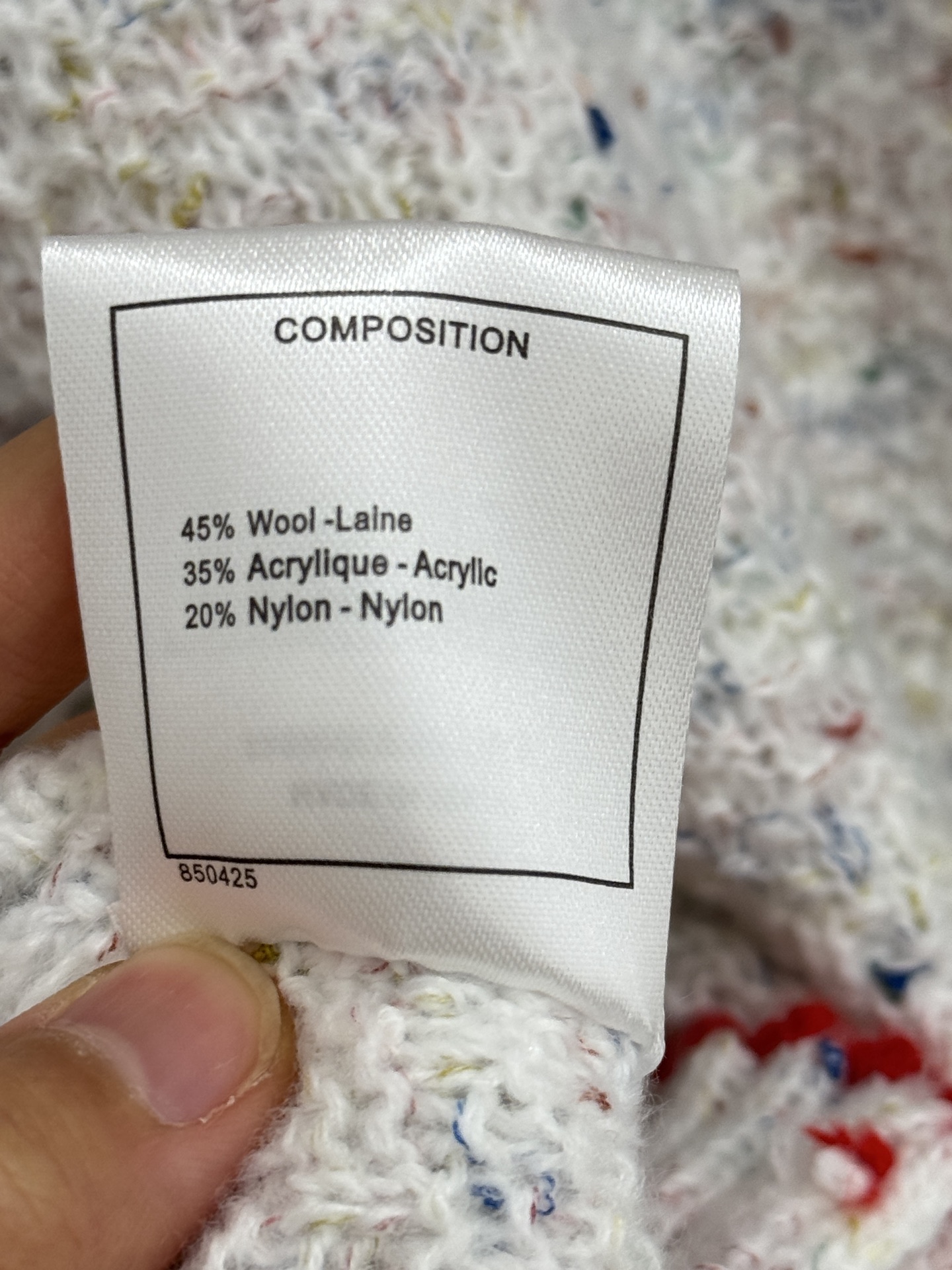 Chanel 字母针织开衫‌，灰白色混纺针织面料，带有细微的彩色杂点纹理，质感柔软且透气，胸前红色字母提花字体简约