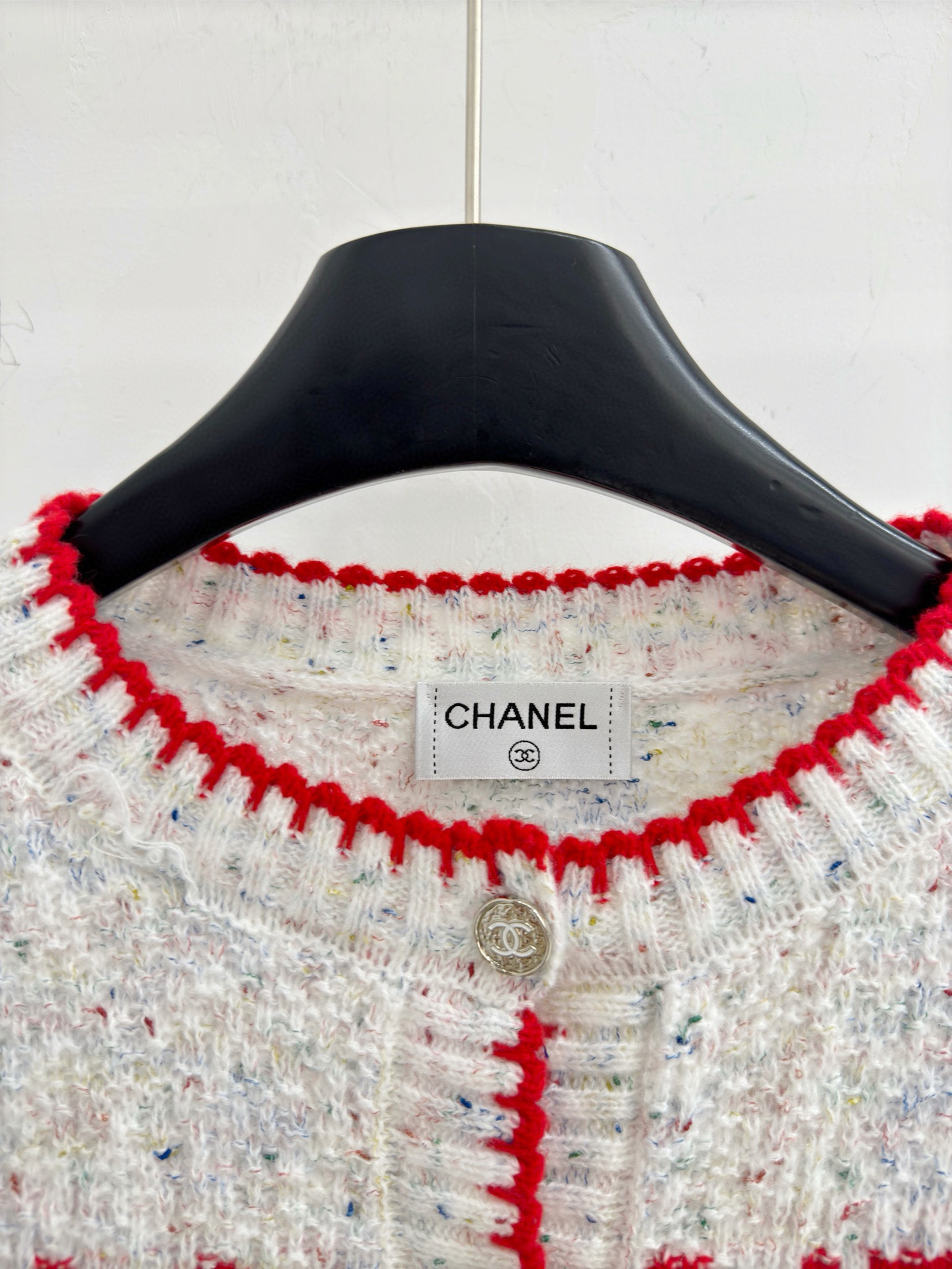 Chanel 字母针织开衫‌，灰白色混纺针织面料，带有细微的彩色杂点纹理，质感柔软且透气，胸前红色字母提花字体简约