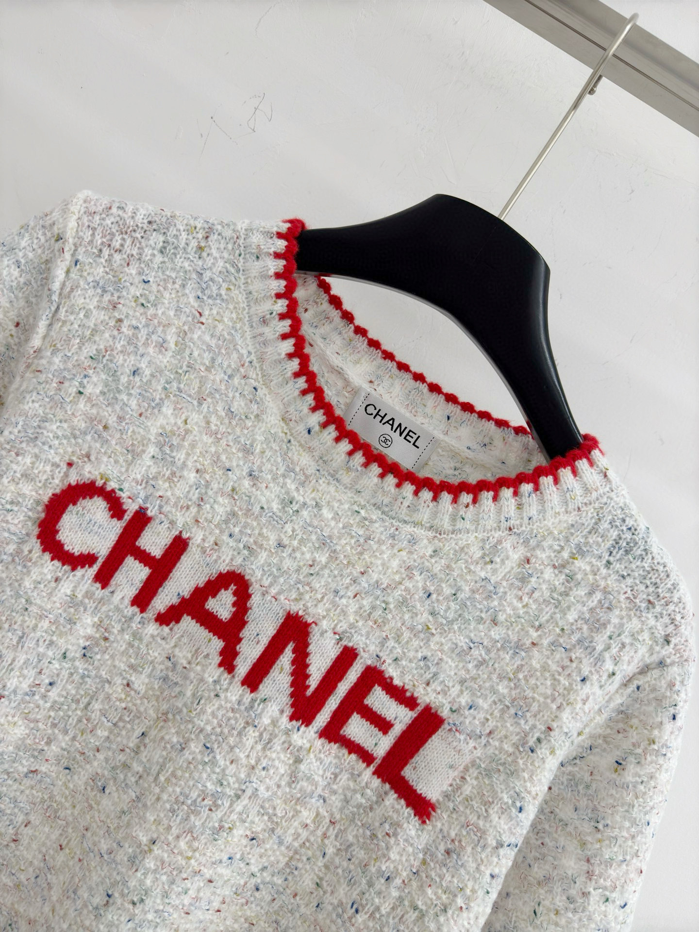 Chanel 字母针织短袖，灰白色混纺针织面料，带有细微的彩色杂点纹理，质感柔软且透气，胸前红色字母提花字体简约