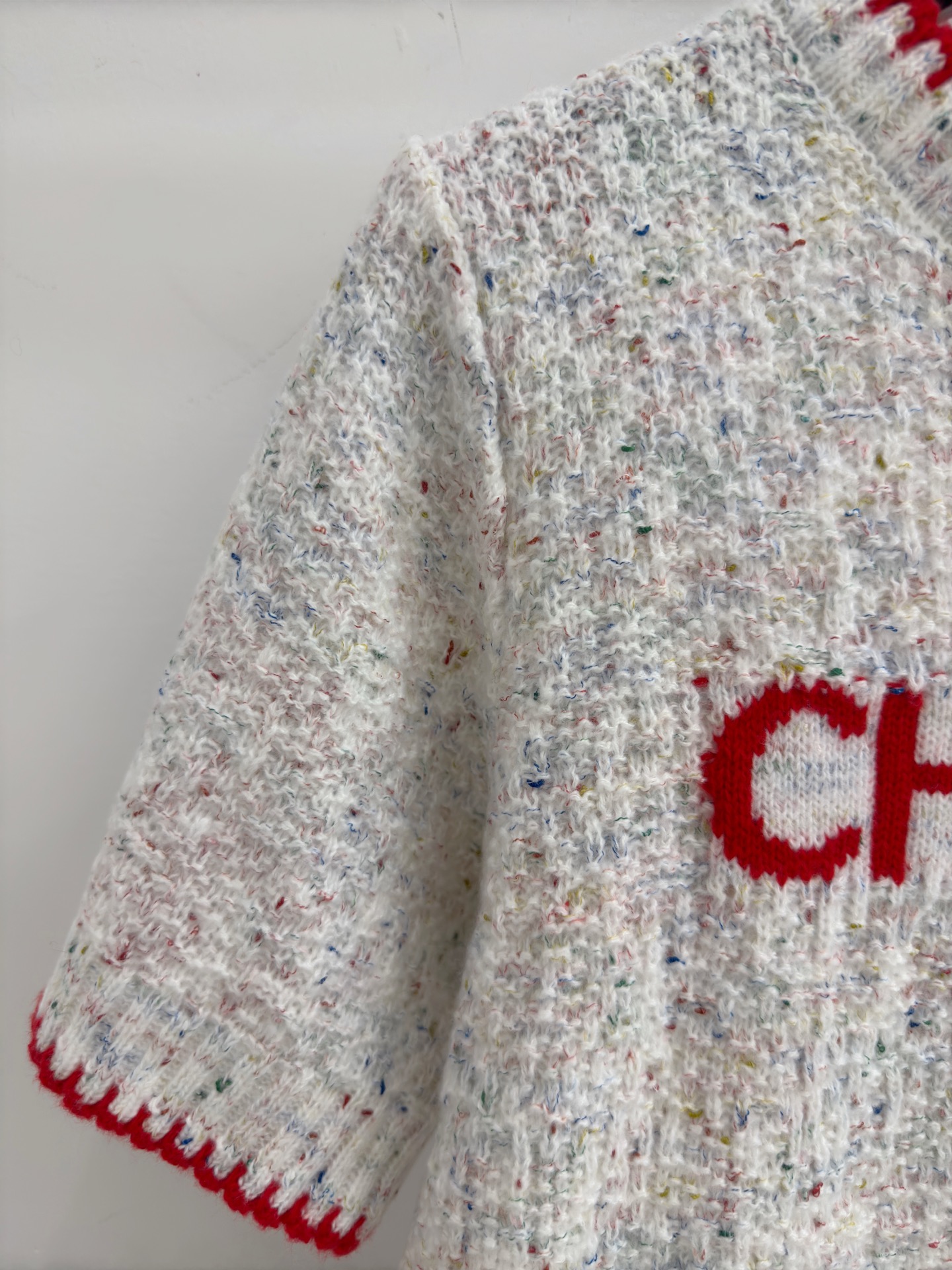 Chanel 字母针织短袖，灰白色混纺针织面料，带有细微的彩色杂点纹理，质感柔软且透气，胸前红色字母提花字体简约