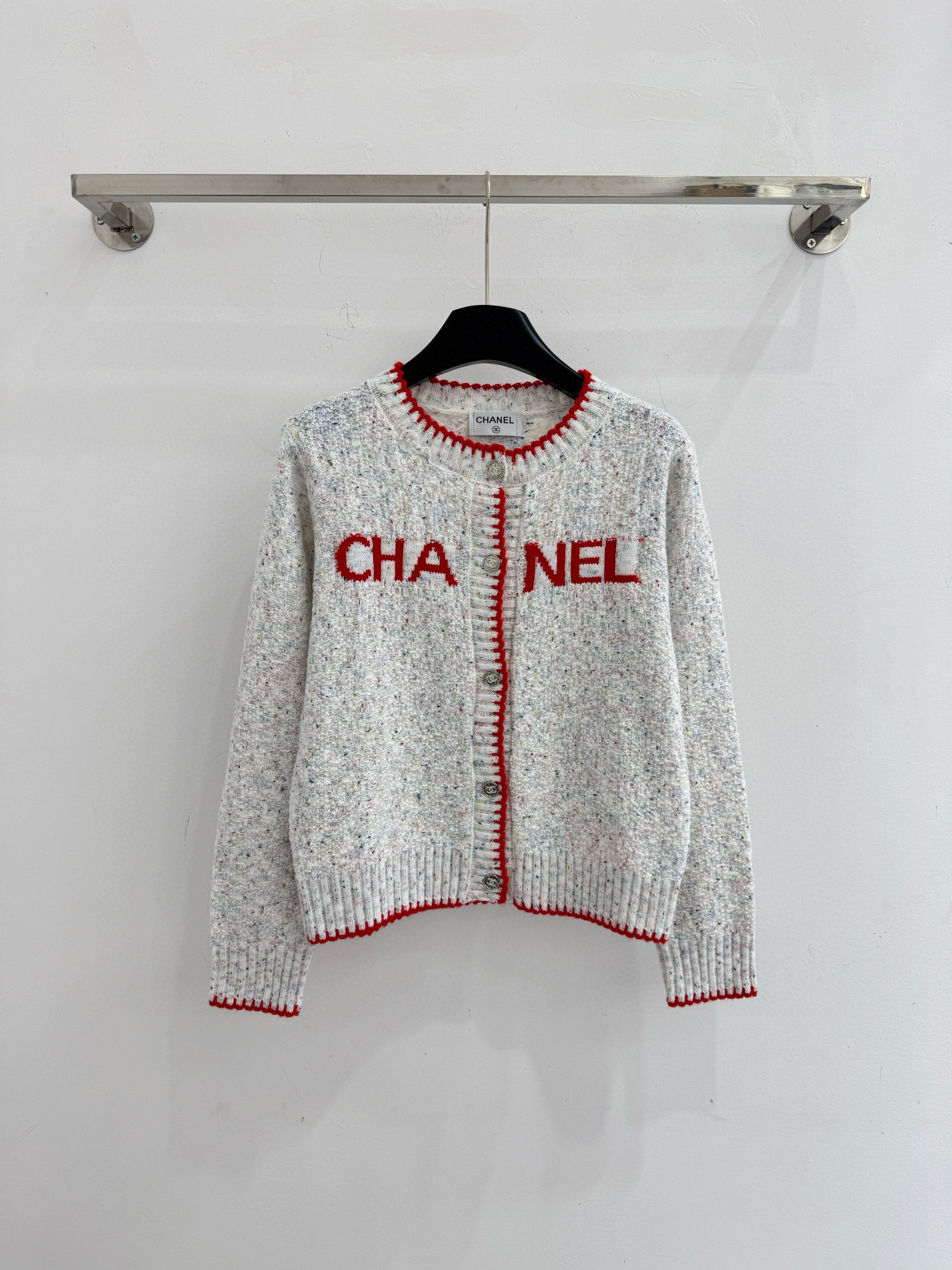 Chanel 字母针织开衫‌，灰白色混纺针织面料，带有细微的彩色杂点纹理，质感柔软且透气，胸前红色字母提花字体简约