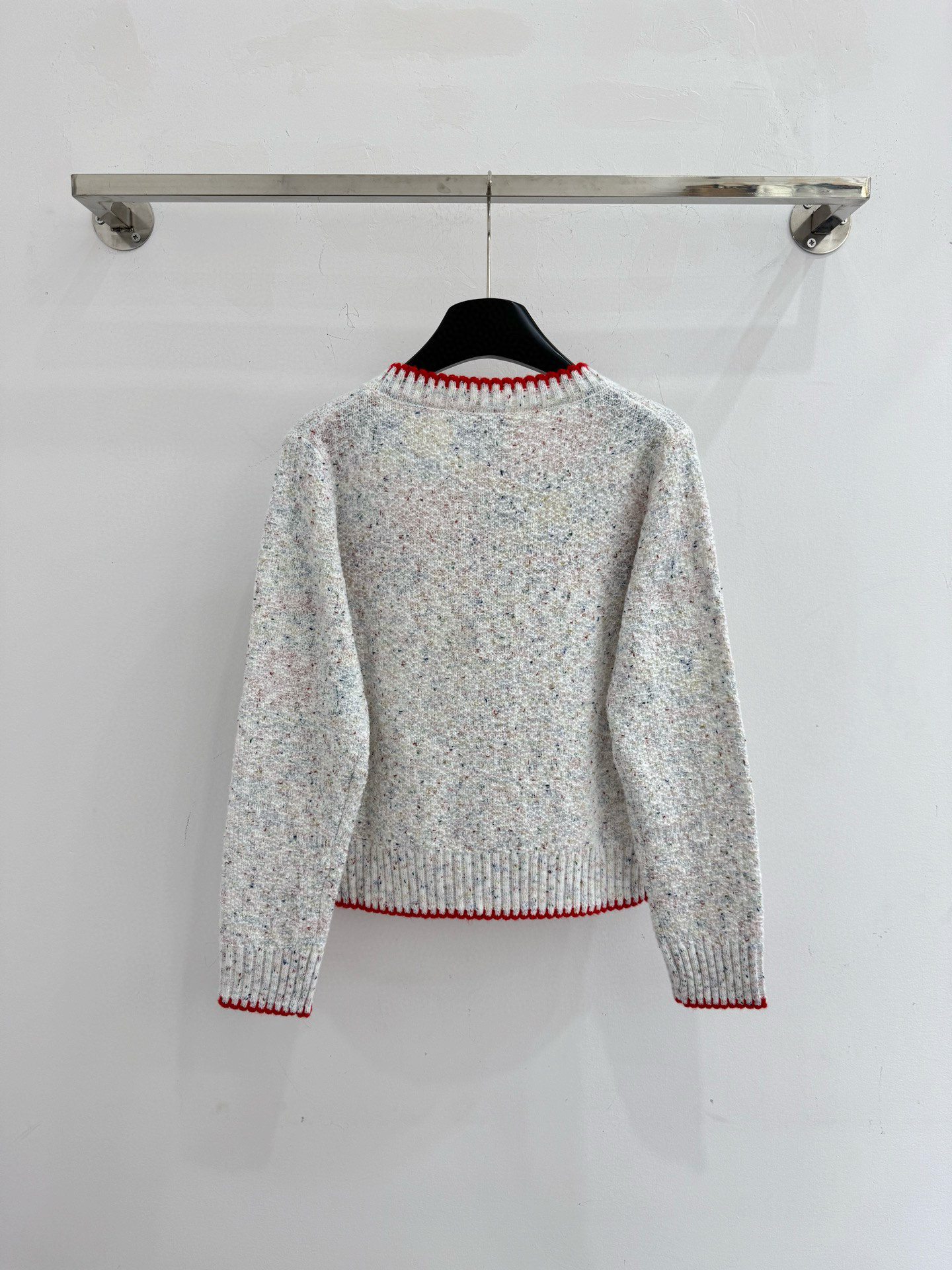 Chanel 字母针织开衫‌，灰白色混纺针织面料，带有细微的彩色杂点纹理，质感柔软且透气，胸前红色字母提花字体简约