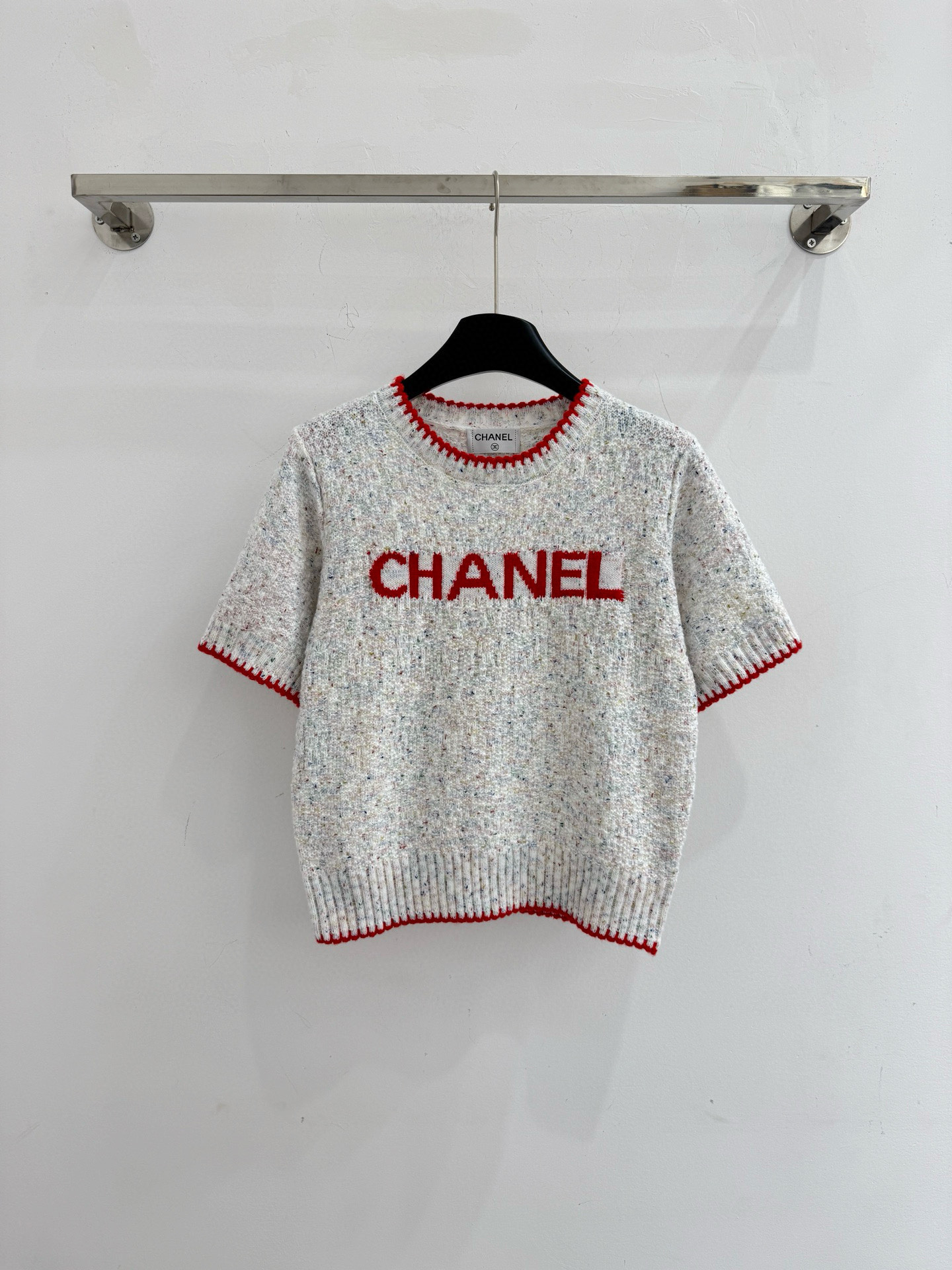 Chanel 字母针织短袖，灰白色混纺针织面料，带有细微的彩色杂点纹理，质感柔软且透气，胸前红色字母提花字体简约