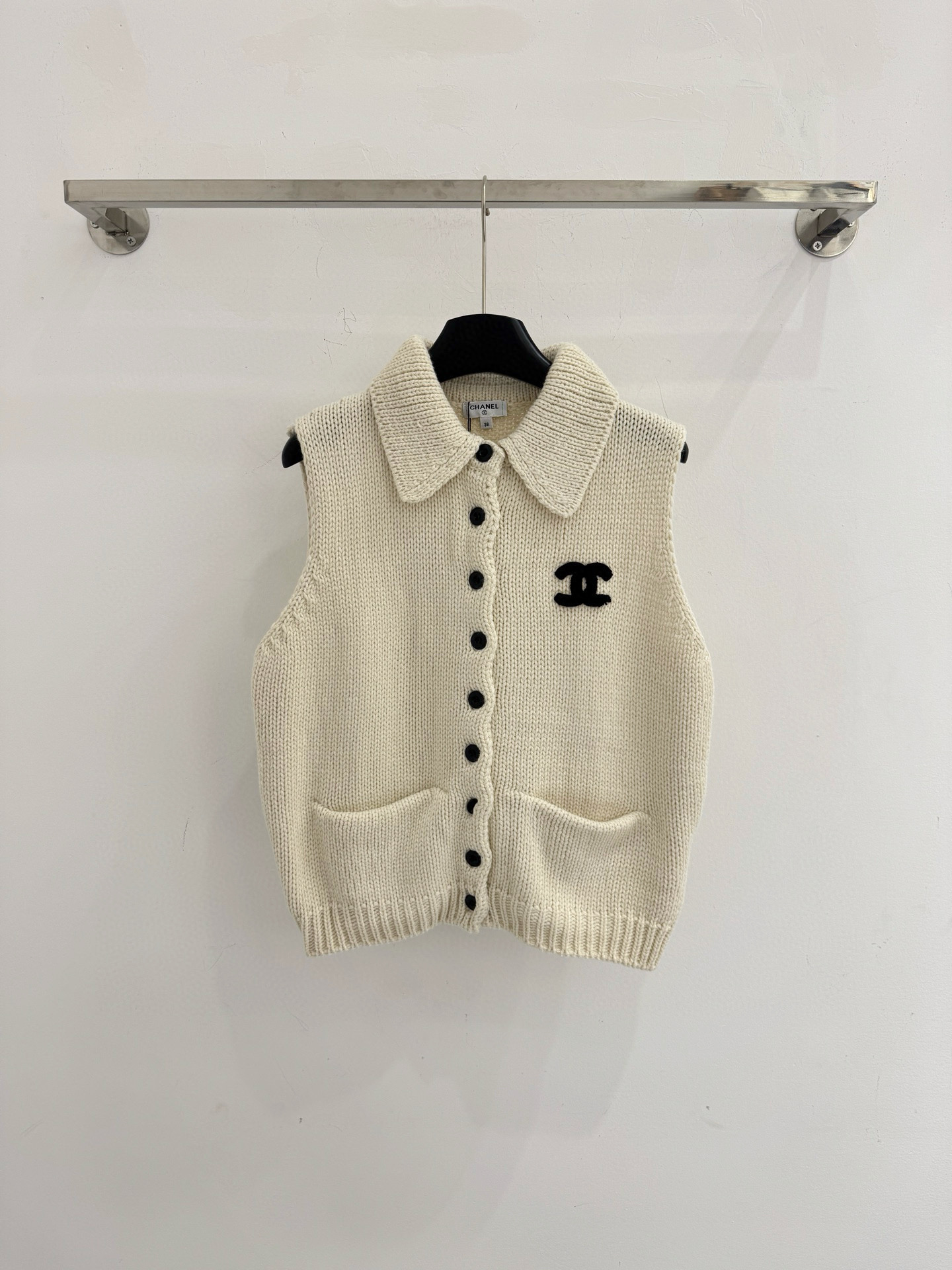 Chanel 无袖坎肩版型，翻领设计，前襟单排黑色圆形纽扣闭合，两侧各有一个对称口袋，简约优雅