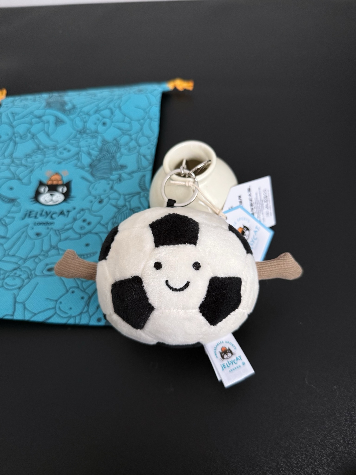 NO:809861,Actual shot | Fun sports football bag charm is an ideal match for match day. The ball is covered with cream hexagonal and black pentagonal plush fabric, with a thumbs up on the suede arms, equipped with a silver hook and Jellycat nameplate, suitable for matching with various wallets and backpacks. This gift is a thoughtful choice for football fans., Jellycat doll trendy department store, wallets, backpacks19860909实拍｜趣味运动足球包包挂饰是比赛日的理想搭配. 球体覆盖着奶油色的六边形和黑色的五边形毛绒面料,绒面手臂上,大拇指竖起,配有银色挂钩和Jellycat铭牌,适合搭配各种钱包和背包.这件礼物是送给足球迷的用心之选.,Jellycat公仔潮品百货,wallets,backpacks,accessory