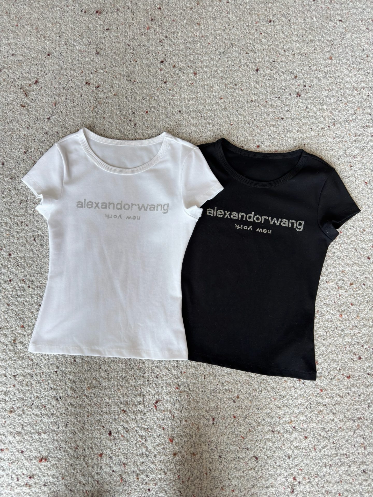 NO:858708,Designer [26 new summer fashionable hot girl design, round neck short-sleeved T-shirt with rhinestoned letters on the front and back, slimming trend] This is an Alexander Wang style slim T-shirt with a 'high-end sense of relaxation', which perfectly captures the neatness of the American hot girl. The high-elastic fabric of 93 cotton + 7 spandex is selected, which is soft and fufu and has its own shaping power. The upper body outlines a smooth waist and abdomen line in one second, making it look slim but not tight.  The hot diamond brand logo on the front is low-key and eye-catching, while the radial letter print on the back hides ingenuity. The basic model can also be worn with a fashionable feel without clashing. Both black and white are 'evergreen styles' in the wardrobe. Wearing them alone with a denim skirt is sweet and cool. Paired with suit pants, it can instantly transform into a casual and sophisticated style for commuting. It is versatile and can easily provide you with inspiration for the whole summer. SML,,skirts,T-shirt,tees,t-shirt,business suit,19860909设计师【26夏季新款时髦辣妹设计前后字母烫钻圆领短袖T恤显瘦上衣潮】 这是一件自带「高阶松弛感」的Alexander Wang风修身T恤,把美式辣妹的利落感拿捏得刚刚好. 精选93棉+7氨纶的高弹面料,软fufu的同时又自带塑形力,上身一秒勾勒出流畅的腰腹线条,显瘦又不勒肉. 正面的烫钻品牌标识低调吸睛,背后放射状的字母印花则暗藏巧思,基础款也能穿出不撞款的时髦感.黑白两色都是衣柜里的“常青款”,单穿配牛仔裙是甜酷辣妹,搭西装裤又能秒变通勤轻熟风,百搭不出错,轻松承包你一整个夏天的穿搭灵感. SML,,skirts,T-shirt,tees，t-shirt,business suit,,Women's clothing