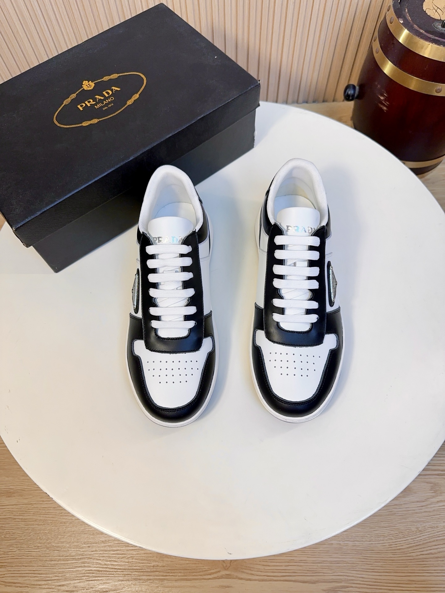 NO:834015,Prada is a top luxury brand founded in Milan, Italy in 1913. It subverts traditional avant-garde designs and is recognized as a 'style definer' in the fashion industry. Prada's shoe series, especially sports shoes, has always been the benchmark in the high-end casual shoe market.  The main body of the shoe upper is made of first-layer calfskin imported from Italy. It has been treated with the brand's exclusive tanning process. The leather surface is fine and shiny, has high flexibility, is not easy to wrinkle and crack, and can maintain the firm shape of the shoe even after long-term wear. It has a high-grade touch and is skin-friendly and does not abrade the feet.  The black part of the black and white model and the silver part of the silver and white model are also made of top-grain cowhide of the same grade. The silver model is also treated with a special metallic mirror coating, which has a high-grade luster, and the coating is wear-resistant and not easy to oxidize. The breathable perforated area of ​​the toe, while maintaining the leather texture, improves breathability and avoids stuffy feet. The tongue is made of skin-friendly leather and is printed with hot stamped Prada Milano words; the lining of the shoe mouth is soft, reducing friction when wearing and improving comfort.  The entire shoe is made of skin-friendly sheepskin lining, which is soft to the touch, reduces friction when wearing, and improves overall durability. The brand-customized cushioning sheepskin insole, with the Prada logo, is soft and supportive, which can effectively relieve foot fatigue after long walks, and is removable for easy cleaning and care.  The sole is a lightweight rubber midsole with a moderate thickness and a slight heightening effect (about 2-3cm). It has both lightweight and cushioning properties. It will not tire your feet after long-term wear. The non-slip and wear-resistant rubber outsole has the Prada embossed logo and anti-slip texture. It has strong grip, no matter it is raining.  It can provide stable support on wet or slippery roads, and its wear resistance can also meet the needs of daily commuting and short-distance travel. 38-44, A9,, prada, prada, sneakers, cowhide, sheepskin19860909Prada（普拉达）是1913年创立于意大利米兰的顶级奢侈品牌,以颠覆传统的先锋设计,是时尚界公认的“风格定义者”.Prada的鞋履系列,尤其是运动鞋,一直是高端休闲鞋市场的标杆. 鞋面主体采用意大利进口头层小牛皮,经过品牌专属鞣制工艺处理,皮面细腻有光泽,柔韧度高,不易起皱、开裂,长期穿着也能保持鞋型挺括,触感高级且亲肤不磨脚. 黑白款的黑色部分、银白款的银色部分,同样采用同等级头层牛皮,银色款还做了特殊的金属镜面涂层处理,自带高级光泽感,且涂层耐磨不易氧化.鞋头的透气打孔区域,在保持皮革质感的同时,提升了透气性,避免闷脚. 鞋舌采用亲肤皮革材质,印有烫金Prada Milano字样；鞋口内衬柔软,减少穿着时的摩擦感,提升舒适度. 全鞋采用亲肤羊皮内里,触感柔软,减少穿着时的摩擦感,同时提升整体的耐用性.品牌定制的缓震羊皮鞋垫,带有Prada标识,柔软有支撑,能有效缓解久走的足部疲劳,且可拆卸设计方便清洁打理. 鞋底轻质橡胶中底,厚度适中,自带轻微增高效果（约2-3cm）,兼具轻量化和缓震性能,久穿不累脚,防滑耐磨橡胶大底,带有Prada压花徽标和防滑纹路,抓地力强,无论是雨天还是湿滑路面都能提供稳定支撑,耐磨性也能满足日常通勤、短途出行的需求.38-44,A9,,prada,prada,sneakers,cowhide,sheepskin,Men's shoes