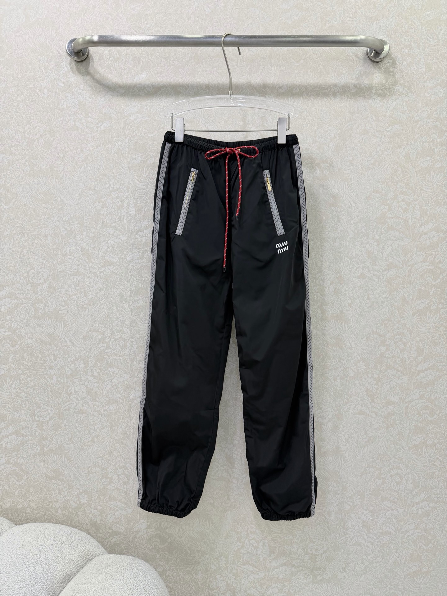 NO:744617,miumi*26 new side webbing leg casual pants, an iconic item of miu style!  Gray webbing is spliced on both sides of the trousers, with delicate zigzag patterns on the edges, visually elongating the legs vertically and enhancing the sporty and casual feel. The front pockets are equipped with customized gold zippers, which enhance the light luxury texture, are both practical and decorative, and are convenient for placing small items. Elastic waistband + contrasting colors  The drawstring design (blue and white drawstrings for the navy model, red and white drawstrings for the black model) is easy to put on and take off without picking up the waistline, adding a sense of liveliness. Loose trousers + ankle cuff design hides fat and looks slimmer, is friendly to various leg types, and creates a casual and lazy atmosphere. The pants are printed with a white 'miu'  The mi*' letter logo highlights the style attributes in a low-key manner and is highly recognizable. 2 colors and 3 codes SMLR, Miu Miu-clothing, miumiu,19860909miumi*26新款侧织带束脚休闲裤 miu系穿搭的标志性单品！裤身两侧拼接灰色织带,边缘带有精致锯齿纹,视觉上纵向拉长腿型,同时强化运动休闲感.前侧口袋配有定制金色拉链,提升轻奢质感,兼具实用性与装饰性,方便放置小物件.松紧腰头+撞色抽绳设计（藏蓝款为蓝白抽绳,黑色款为红白抽绳）,穿脱方便且不挑腰围,增加活泼感.宽松裤型+束脚口设计,藏肉显瘦,对各种腿型友好,同时营造出随性慵懒的氛围.裤身印有白色“miu mi*”字母标识,低调点明风格属性,辨识度拉满. 2色3码SMLR,缪缪-服装,miumiu,,Women's clothing
