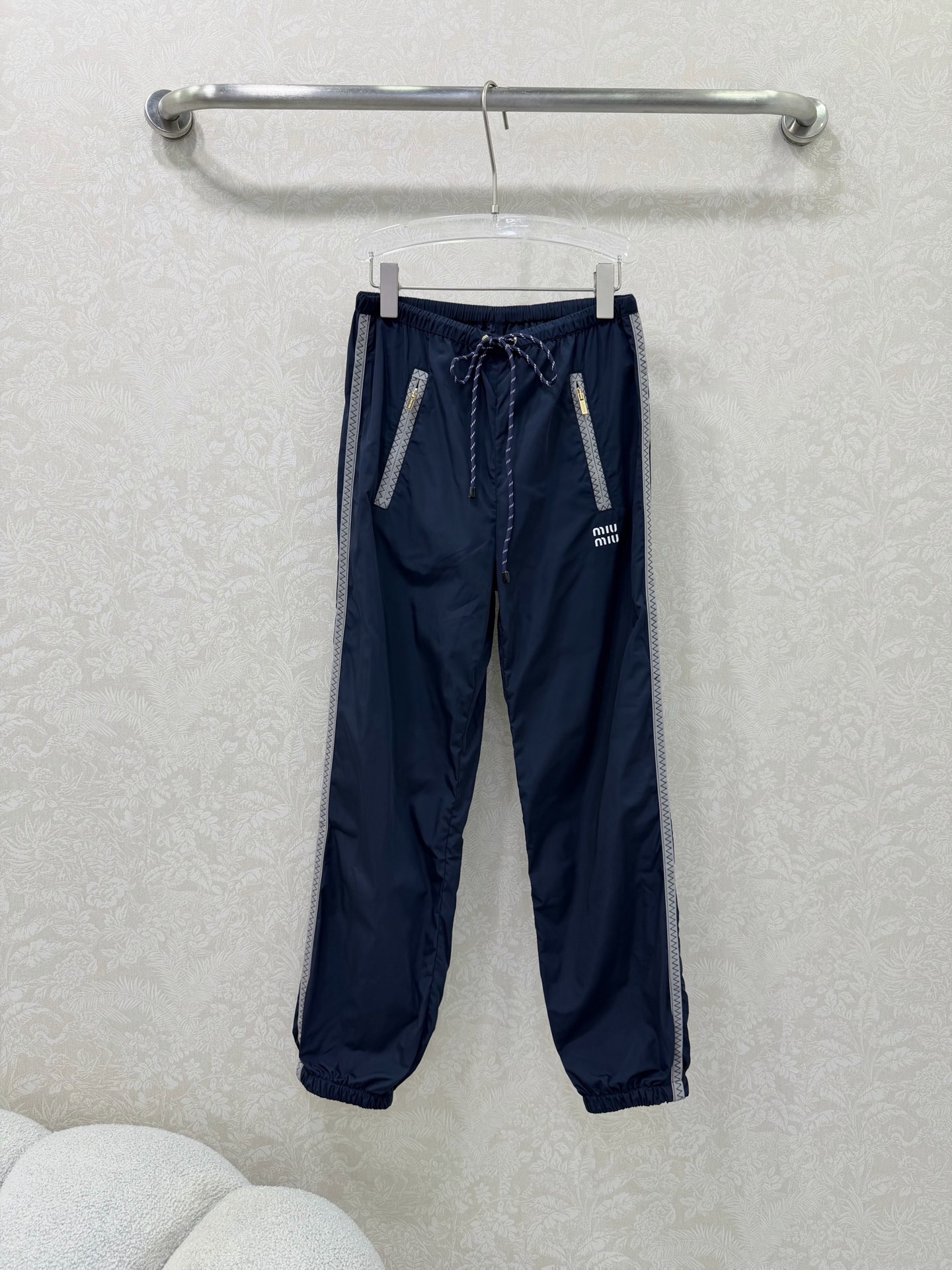 NO:744632,miumi*26 new side webbing leg casual pants, an iconic item of miu style!  Gray webbing is spliced on both sides of the trousers, with delicate zigzag patterns on the edges, visually elongating the legs vertically and enhancing the sporty and casual feel. The front pockets are equipped with customized gold zippers, which enhance the light luxury texture, are both practical and decorative, and are convenient for placing small items. Elastic waistband + contrasting colors  The drawstring design (blue and white drawstrings for the navy model, red and white drawstrings for the black model) is easy to put on and take off without picking up the waistline, adding a sense of liveliness. Loose trousers + ankle cuff design hides fat and looks slimmer, is friendly to various leg types, and creates a casual and lazy atmosphere. The pants are printed with a white 'miu'  The mi*' letter logo highlights the style attributes in a low-key manner and is highly recognizable. 2 colors and 3 codes SMLR, Miu Miu-clothing, miumiu,19860909miumi*26新款侧织带束脚休闲裤 miu系穿搭的标志性单品！裤身两侧拼接灰色织带,边缘带有精致锯齿纹,视觉上纵向拉长腿型,同时强化运动休闲感.前侧口袋配有定制金色拉链,提升轻奢质感,兼具实用性与装饰性,方便放置小物件.松紧腰头+撞色抽绳设计（藏蓝款为蓝白抽绳,黑色款为红白抽绳）,穿脱方便且不挑腰围,增加活泼感.宽松裤型+束脚口设计,藏肉显瘦,对各种腿型友好,同时营造出随性慵懒的氛围.裤身印有白色“miu mi*”字母标识,低调点明风格属性,辨识度拉满. 2色3码SMLR,缪缪-服装,miumiu,,Women's clothing