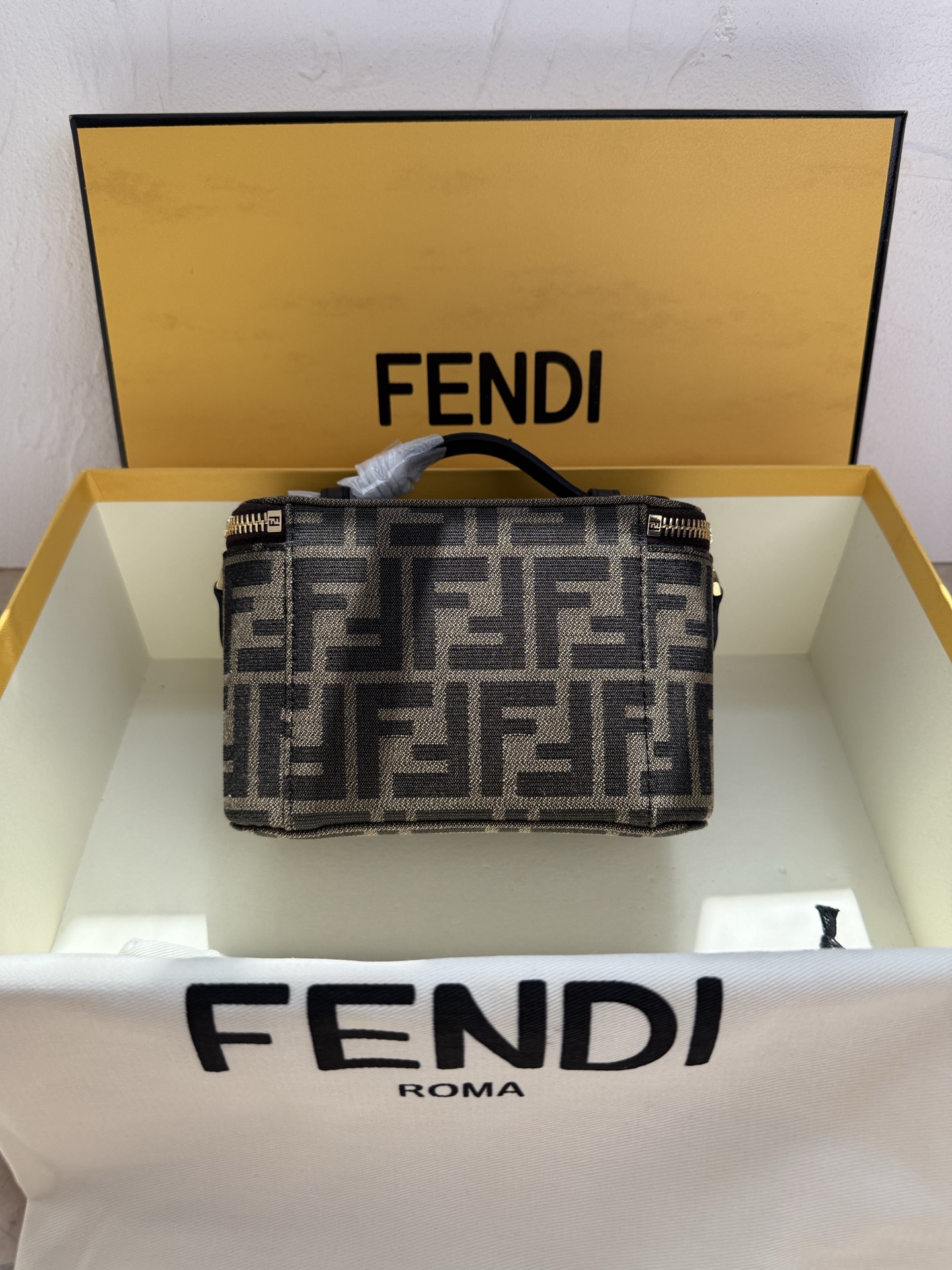 Fendi 廓形挺立的小巧型Vanity手袋采用双滑动拉链开合设计，饰有FF细节和皮革拉链头。烟草棕FF提花布料材质