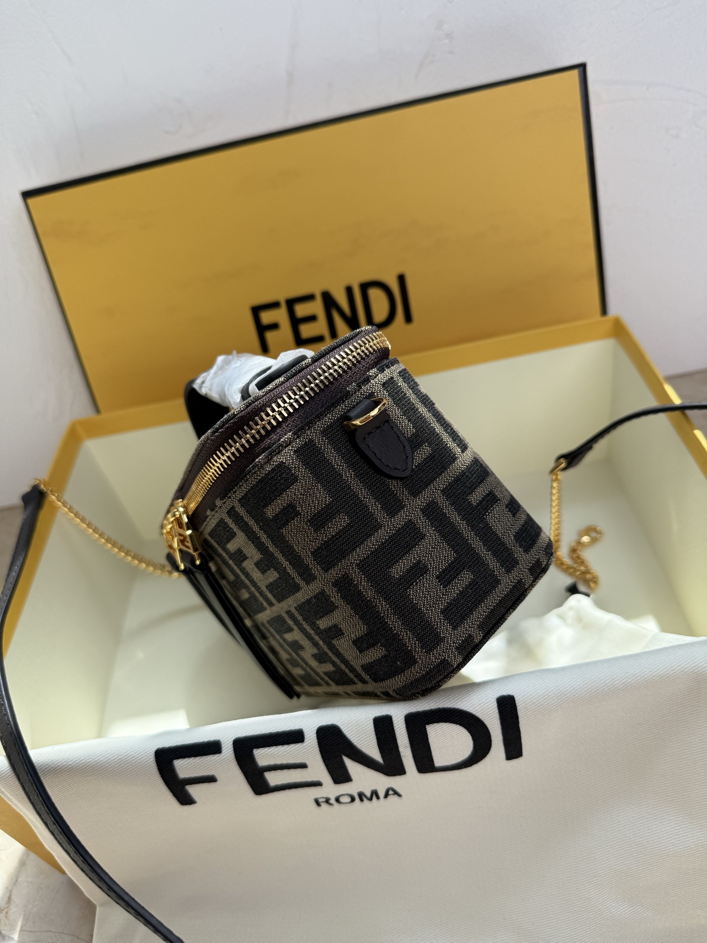 Fendi 廓形挺立的小巧型Vanity手袋采用双滑动拉链开合设计，饰有FF细节和皮革拉链头。烟草棕FF提花布料材质