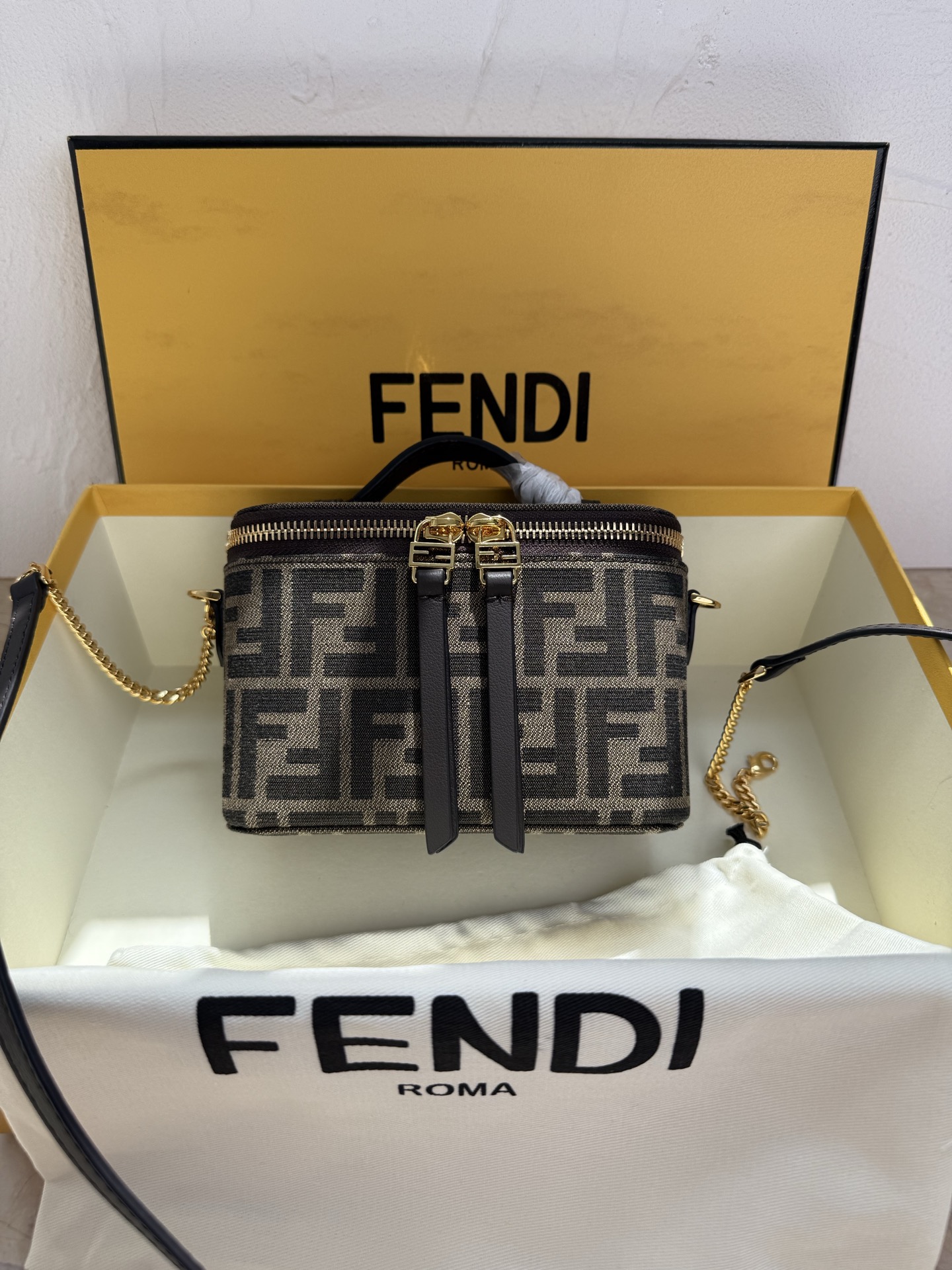 Fendi 廓形挺立的小巧型Vanity手袋采用双滑动拉链开合设计，饰有FF细节和皮革拉链头。烟草棕FF提花布料材质