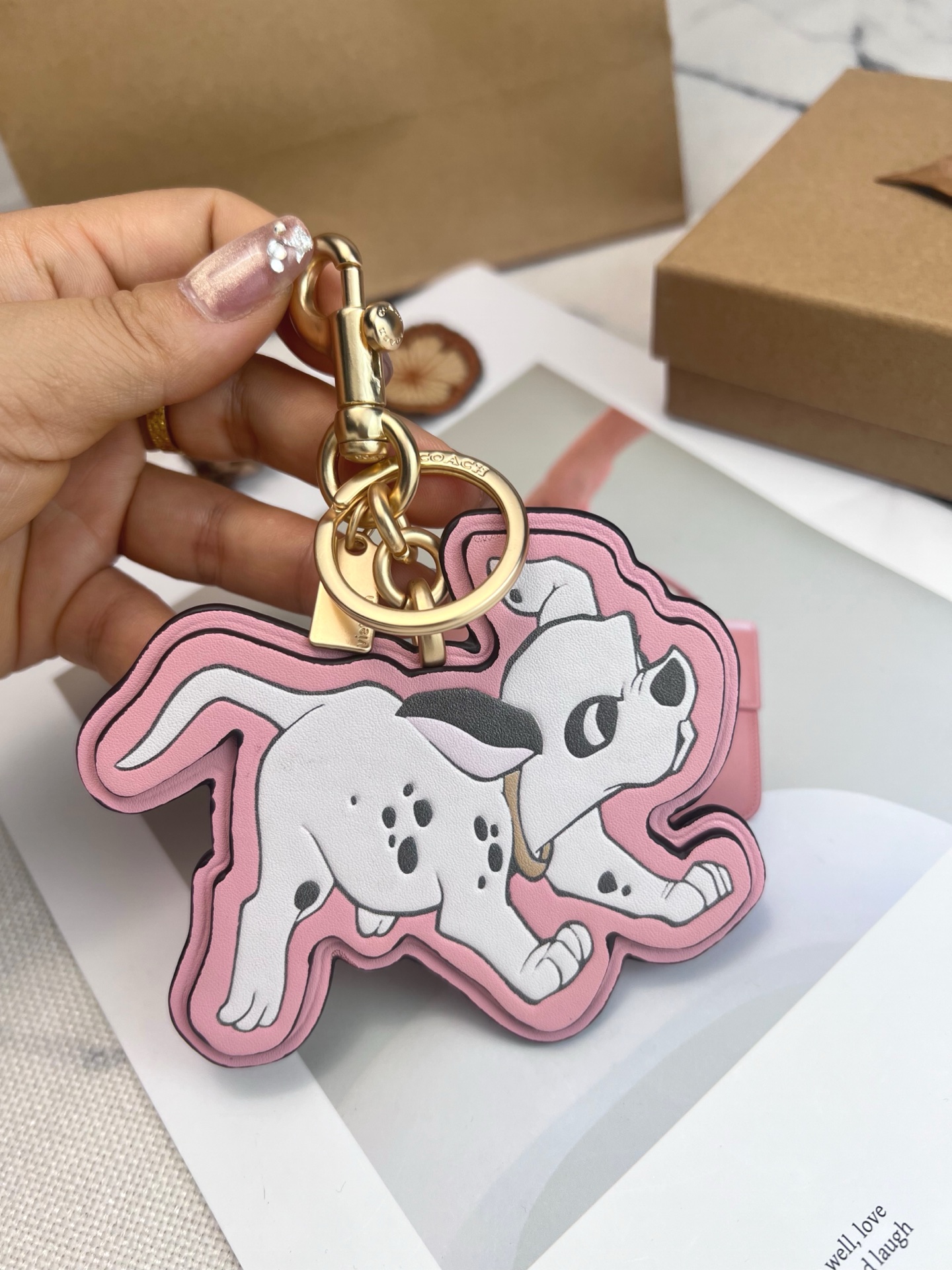 Coach x Disney联名斑点狗挂件，灵感来自《101忠狗》，皮革材质+粉色边框，少女感满满。金属五金连接，适合包包或钥匙扣，小巧可爱，收藏价值高，迪士尼粉丝必入!日常搭配或送礼都超合适门，组细节精致，兼具实用与趣味，出门也能萌趣加分~
尺寸11*9*1cm