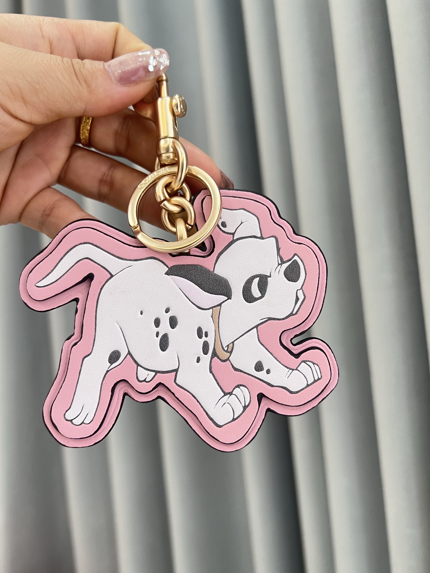 Coach x Disney联名斑点狗挂件，灵感来自《101忠狗》，皮革材质+粉色边框，少女感满满。金属五金连接，适合包包或钥匙扣，小巧可爱，收藏价值高，迪士尼粉丝必入!日常搭配或送礼都超合适门，组细节精致，兼具实用与趣味，出门也能萌趣加分~
尺寸11*9*1cm