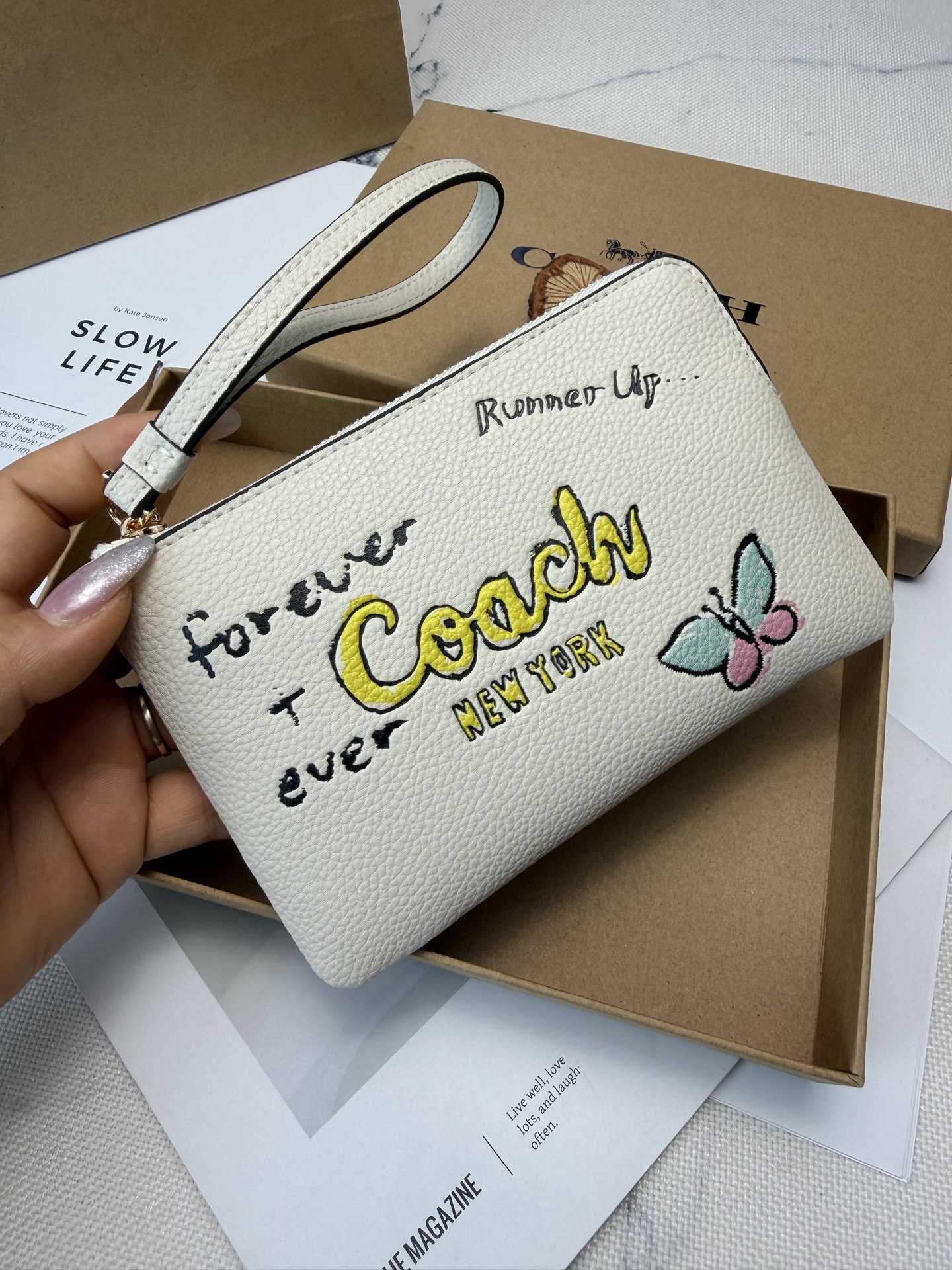 Coach Coach这款CAQ54涂鸦风零钱手拿包 采用白色荔枝纹皮革 手感细腻又耐用