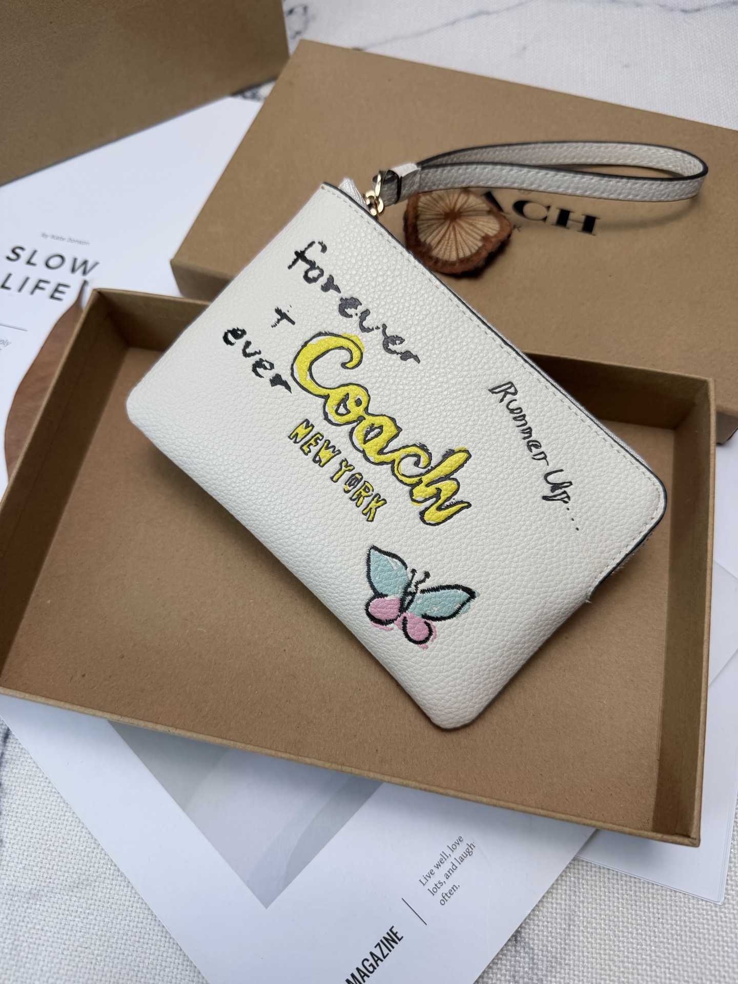 Coach Coach这款CAQ54涂鸦风零钱手拿包 采用白色荔枝纹皮革 手感细腻又耐用