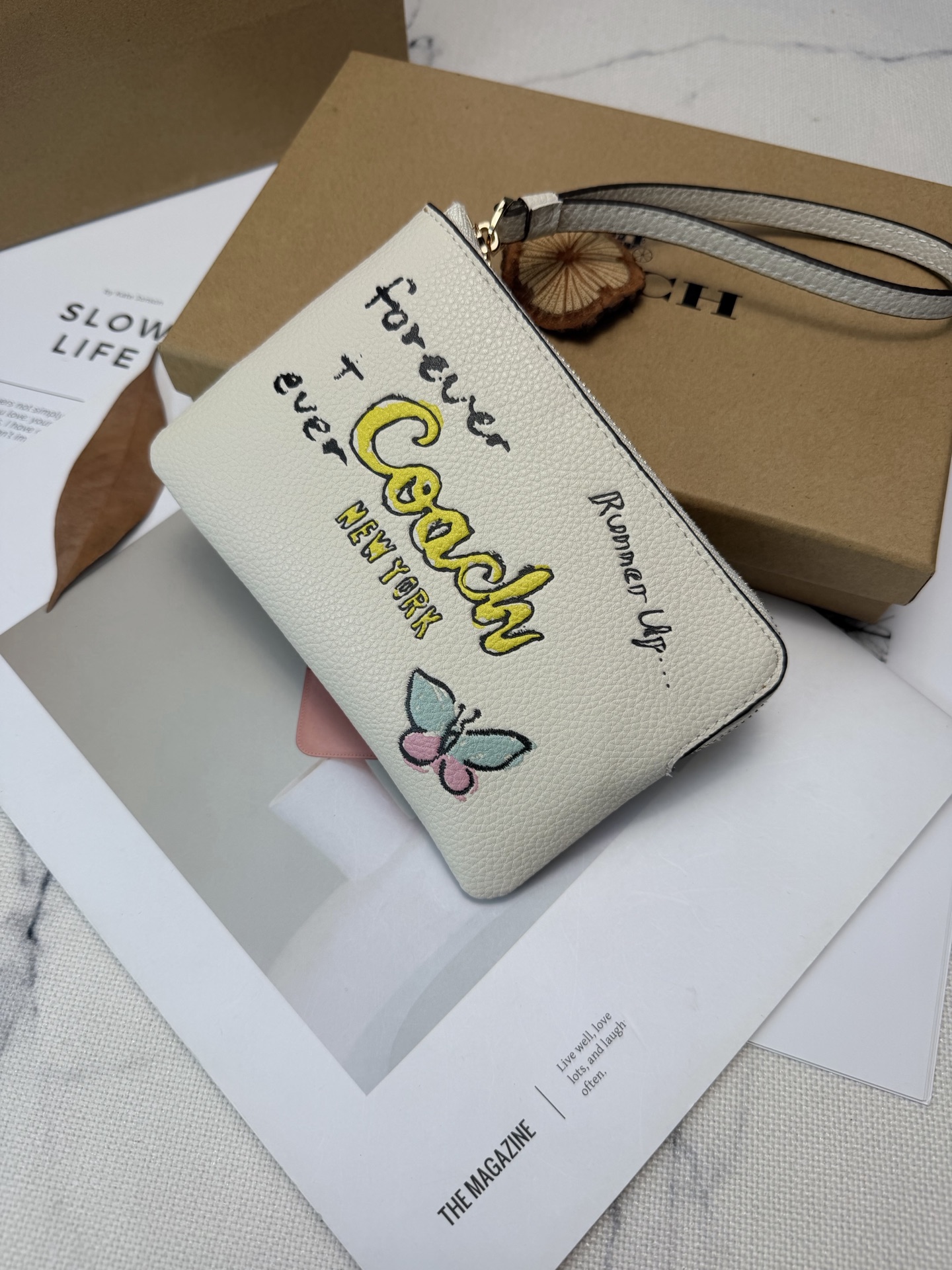 Coach Coach这款CAQ54涂鸦风零钱手拿包 采用白色荔枝纹皮革 手感细腻又耐用
