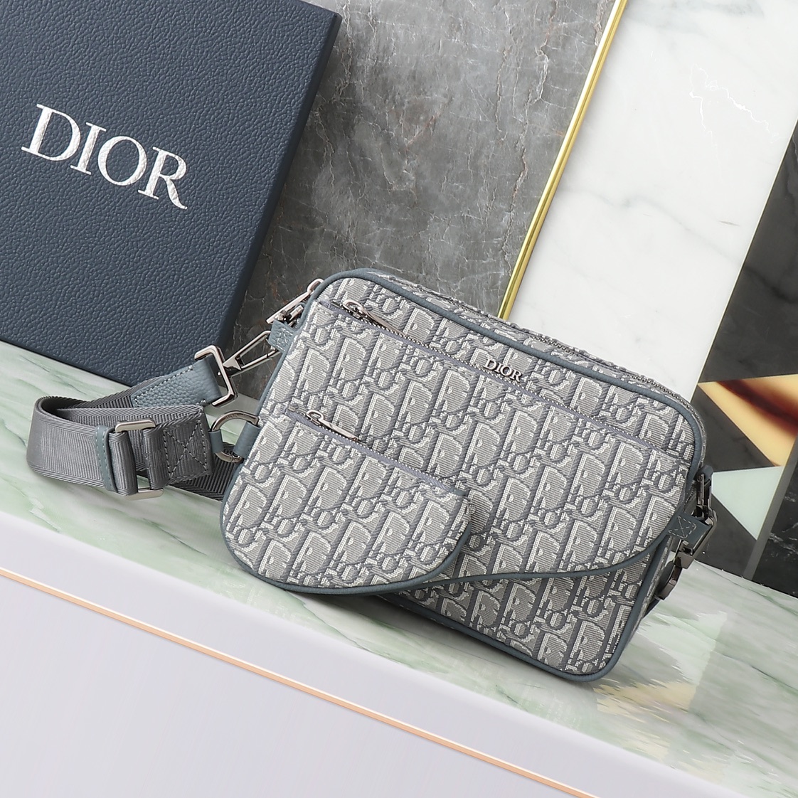 Este bolso de tres piezas tipo silla de montar está confeccionado en tela Oblique de color gris oscuro, llamativo y ver…