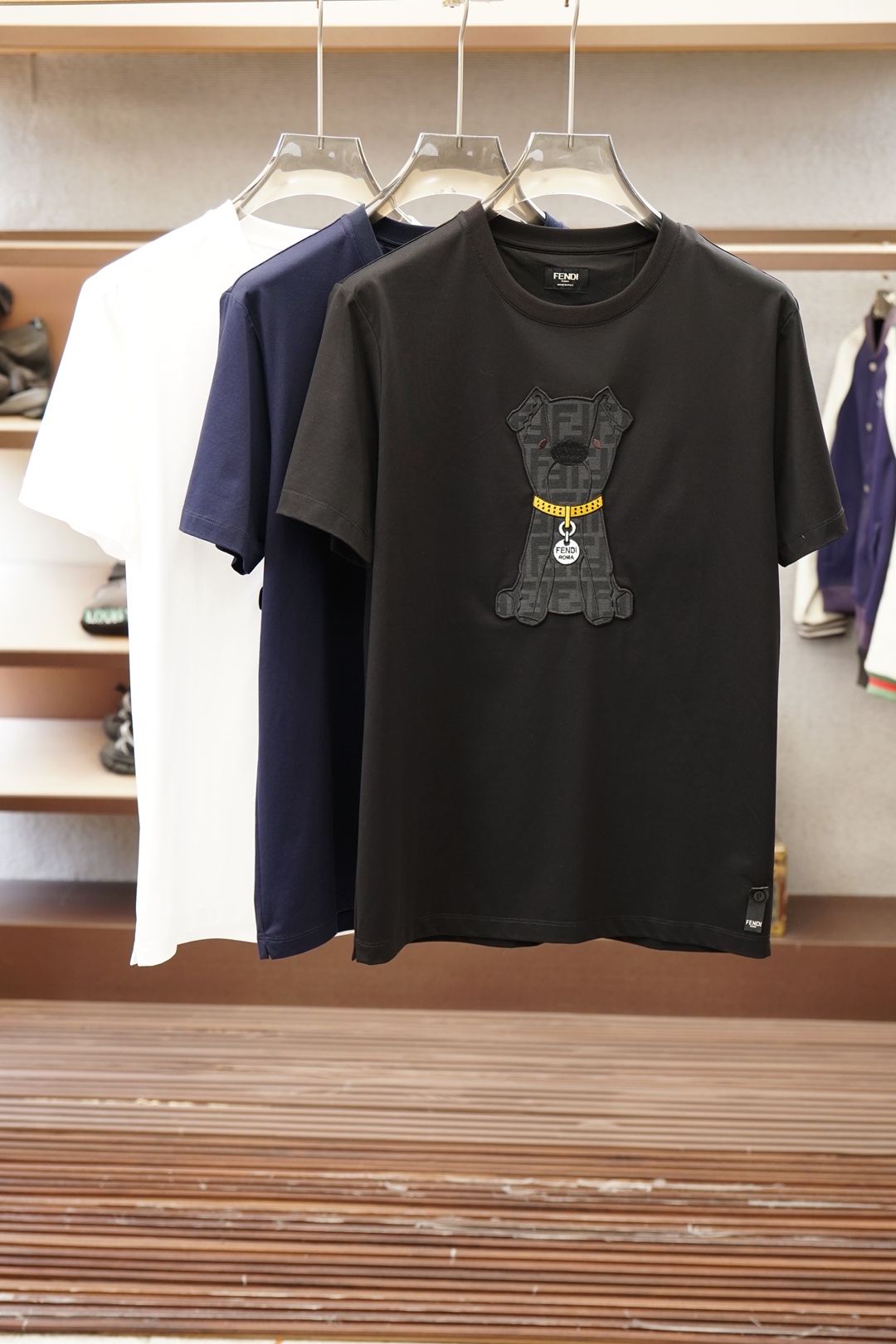 NO:857765,, Fendi Fendi/Product Introduction FF / Cotton T-shirt with patchwork pattern. Fabric: 32-count single-yarn double-sided fabric / 280G. Made of 32-count cotton-polyester blended double-sided fabric, the heavy weight gives it a stiff texture and excellent wrinkle resistance. The 75% cotton guarantees skin-friendliness and breathability, and the addition of 25% polyester significantly improves the durability and morphological stability of the fabric. It can still maintain the original shape after multiple washes. The core decoration is realized through three processes. First, the FF logo is woven into a brown base using jacquard weaving technology to form a permanent three-dimensional pattern; then the main visual hierarchy is built through appliqué positioning; and finally, precision hemming is done with needle embroidery, achieving seamless edge solidification through a density of 16 stitches per inch, while enhancing the clarity of the pattern outline. The standard slim fit strikes a balance between showing the body lines and retaining room for movement. The neckline, cuffs and hem are all made of double-needle interlocking technology, which significantly improves the seam strength and wear resistance, ensuring that the item remains in its best condition after long-term wear.,,fendi,fendi,tees,t-shirt,19860909,Fendi芬迪/产品简介 FF / 贴布图案棉质T恤 面料32支单纱双面布 / 280G 采用32支棉涤混纺双面布,重磅克重成就其立挺骨感与卓越抗皱性.75棉质保障亲肤透气,25涤纶的加入则显著提升面料耐久度与形态稳定性,经多次洗护仍能保持初始版型. 核心装饰通过三重工序实现先以提花织造技术将FF标识与棕色基底织为一体,形成永久立体图案；再通过贴布绣定位构建主视觉层次；最后以挨针绣精密包边,通过每英寸16针的密度实现边缘无缝固化,同时强化图案轮廓的清晰度. 标准修身剪裁在展现身体线条与保留活动余量间取得平衡.领口、袖口及下摆均采用双针绷缝工艺,显著提升接缝强度与耐磨度,确保单品在长期穿着后仍维持最佳状态.,,fendi,fendi,tees，t-shirt,,Men's clothing