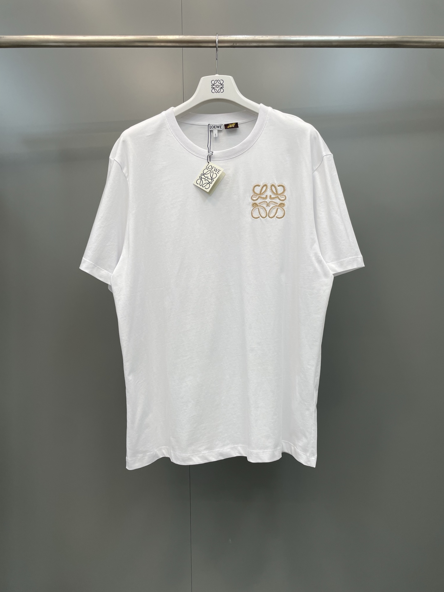 NO:822247,Loewe 26ss new flat embroidered logo short-sleeved T-shirt, selection  Made of 24-count high-count combed cotton, the fabric has a weight of 185G. It has both a delicate skin-friendly feel and an excellent crisp drape. The upper body is breathable and dry, and will not be easily deformed after long-term washing. The round neck is made of ribbed native cloth. The collar has precise hemming technology and excellent stretch resistance. It is not easy to loosen and deform after repeated wear and washing. The iconic Anagram logo on the left side of the body is made with flat embroidery technology, using double-strand metal embroidery thread + natural white cotton.  The threads are outlined in contrasting colors, the density of the embroidery threads is high, and the threads are neat and full. There are no skipped stitches or raw edges on the edges of the pattern, which is both three-dimensional and recognizable. The ready-made garments are cut in an Oversized silhouette, and the dropped shoulder sleeves are designed to modify the shoulder line. The hem is hemmed with double-needle flat stitching technology, and the overall threading is smooth and smooth., Loewe-clothing, loewe, versace, T-shirt, tees, t-shirt,19860909罗意威26ss新款平绣徽标短袖T恤,甄选 24支高支精梳棉打造,面料克重为185G,兼具细腻亲肤的触感与优良的挺括垂坠感,上身透气干爽,久洗不易变形；圆领处采用罗纹本布包边领,领口锁边工艺精密,抗拉伸性优异,反复穿洗不易松垮变形.衣身左侧标志性的Anagram徽标,采用平绣工艺打造,以双股金属绣线+本白棉线撞色勾勒,绣线密度高、走线工整饱满,图案边缘无跳针、毛边,立体感与辨识度兼具.成衣采用Oversized廓形剪裁,落肩袖设计修饰肩线,下摆采用双针平缝工艺锁边,整体走线平整顺滑.,罗意威-服装,loewe,versace,T-shirt,tees，t-shirt,,Women's clothing