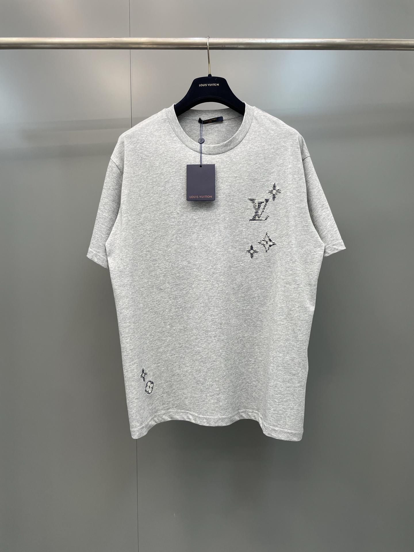 NO:822217,Lujia 26ss new embroidered round neck short-sleeved T-shirt,  The version adopts a slightly loose straight cut, and the neckline is a double-needle ribbed round collar. The overlocking process is used to enhance the collar's stretch resistance, making it less likely to loosen and deform after long-term wear. The brand's Monogram logo scattered on the front and back panels is made of precision flat embroidery technology and is embroidered in blue.  The high-twist cotton thread is embroidered through computer plate making, using a unique imitation hand embroidery random stitching technique to simulate the raw edge texture of hand-painted graffiti. The stitches are fine and neat, presenting a layered three-dimensional relief texture on the plain base fabric, breaking the regularity of traditional embroidery.  The cuffs and hem are rolled using flat-turn double-needle hemming, with clean and neat lines. It perfectly integrates the brand's classic elements with modern deconstructed aesthetics, making it both practical and fashionable for daily wear. Louis Vuitton-clothing, louis vuitton, louis vuitton, louis vuitton, T-shirt, tees, t-shirt,19860909驴家26ss新款刺绣圆领短袖T恤, 版型上采用微宽松直身剪裁,领口为双针罗纹圆领,配合锁边工艺强化领型抗拉伸性,久穿不易松垮变形；前后幅散落的品牌Monogram标识采用精密平绣工艺,以蓝色高捻棉线通过电脑制版绣制,采用独特的仿手绣乱针走线技法,模拟手绘涂鸦的毛边肌理,针脚细密工整,在素色底布上呈现出层次丰富的立体浮雕质感,打破传统刺绣的规整感 袖口与下摆采用平车双针卷边处理,线条干净利落,将品牌经典元素与现代解构美学完美融合,兼具日常实穿性与潮流辨识度,路易威登-服装,louis vuitton,louis vuitton,louis vuitton,T-shirt,tees，t-shirt,,Women's clothing
