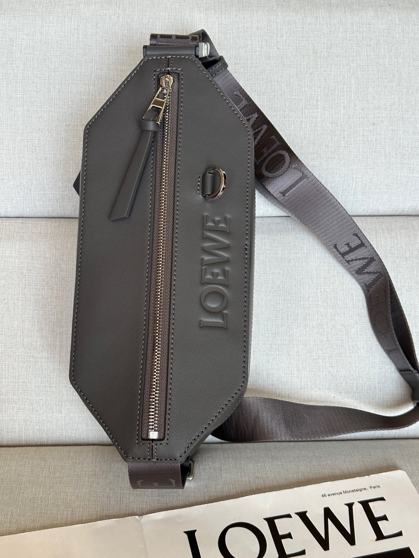 NO:341218,Extra Classic Cowhide Sling Handbag A80 Chocolate (dark gray) Compact Sling Handbag comes with adjustable LOEWE webbing and brand logo metal buckles that can be opened to change the bag capacity and enable multiple ways to carry. External zipper flat pockets improve functionality. This version is made of classic cowhide leather. Can be carried cross-body or as a waist bag. Zipper closure, cowhide zipper head Herringbone cotton canvas lining Embossed with D-ring LOEWE Color (metal accessories): Palladium Material: cowhide Leather Lining: Fabric Weight: 0.4 kg Size: 32.5*9*12.3cm Product model: A80, premium Roewe, loewe, loewe, cowhide19860909特级 经典牛皮革变形 Sling 手袋 A80 巧克力色（深灰） 紧凑型 Sling 手袋配有可调节 LOEWE 织带和品牌标志金属搭扣,可打开以改变手袋容量并实现多种携带方式.外部拉链平口袋进步增强了功能性.这个版本采用经典牛皮革制成. 可斜挎或作为腰包携带. 拉链开合,牛皮革拉链头 人字纹棉质帆布衬里 配有 D 形环的压纹 LOEWE 颜色（金属配件）:钯金色 材质:牛皮革 里料:织物 重量:0.4 kg 尺寸:32.5*9*12.3cm 商品型号:A80,特级罗意威,loewe,loewe,cowhide,Bag