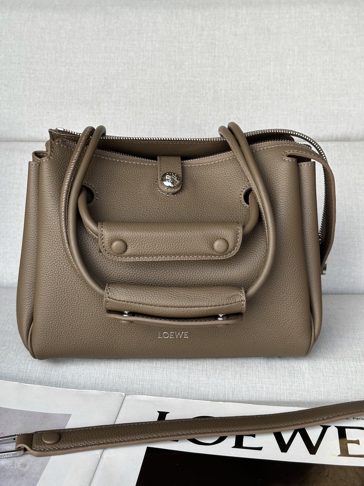 NO:339909,Special Small *0256 Gray Color Size: 23.5*10*19cm Madrid has a soft structural trapezoidal shape, with a gusset design, with adjustable handles and Pebble magnetic buckles. This small version is made of soft cowhide leather. It can be shoulder-mounted, cross-body or hand-mounted Adjustable shoulder straps with leather extension straps Anagram Pebble magnetic buckle closure, zipper closure One zipper inner pocket Anagram Pebble metal foot nails Napa sheepskin lining, special Loewe, cowhide, sheepskin19860909特级 小号*0256 灰谒色 尺寸:23.5*10*19cm Madrid 具有柔软的结构感梯形造型,采用角撑设计,搭配可调节提手和 Pebble 磁扣.此小号版本采用柔软牛皮革制成. 可肩背、斜挎或手提 可调节肩带,搭配皮革延长带 Anagram Pebble 磁扣开合,拉链开合 一个拉链内袋 Anagram Pebble 金属脚钉 纳帕羊皮革衬里,特级罗意威,loewe,cowhide,sheepskin,Bag